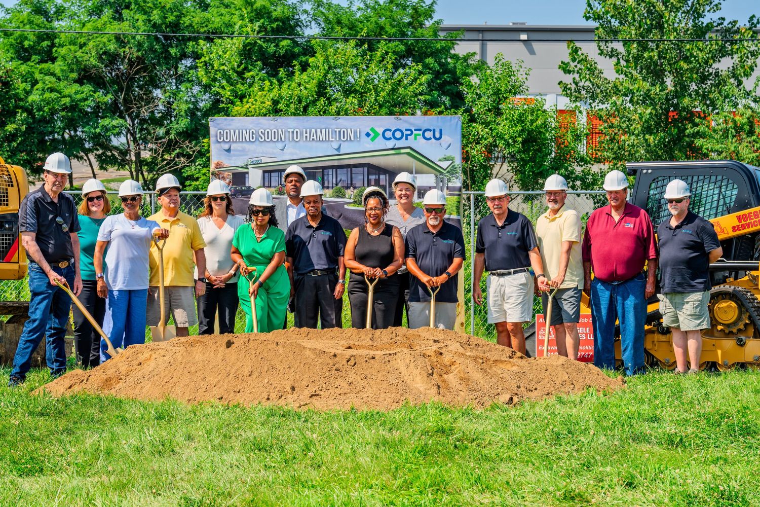 Large group posing with shovels at COPFCU groundbreaking ceremony on a sunny day.