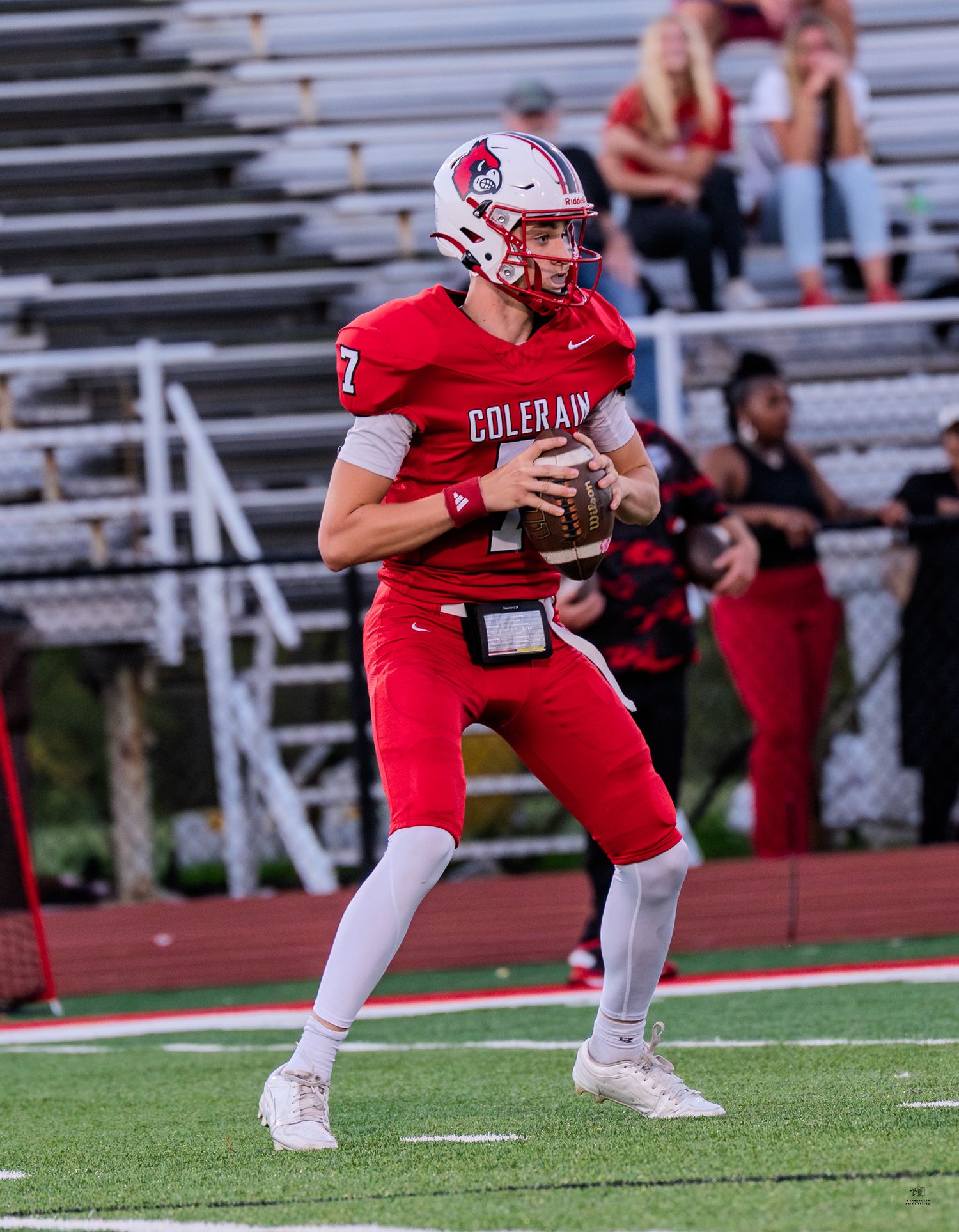 Colerain high school quarterback number 7 in red uniform drops back to pass during a football game.