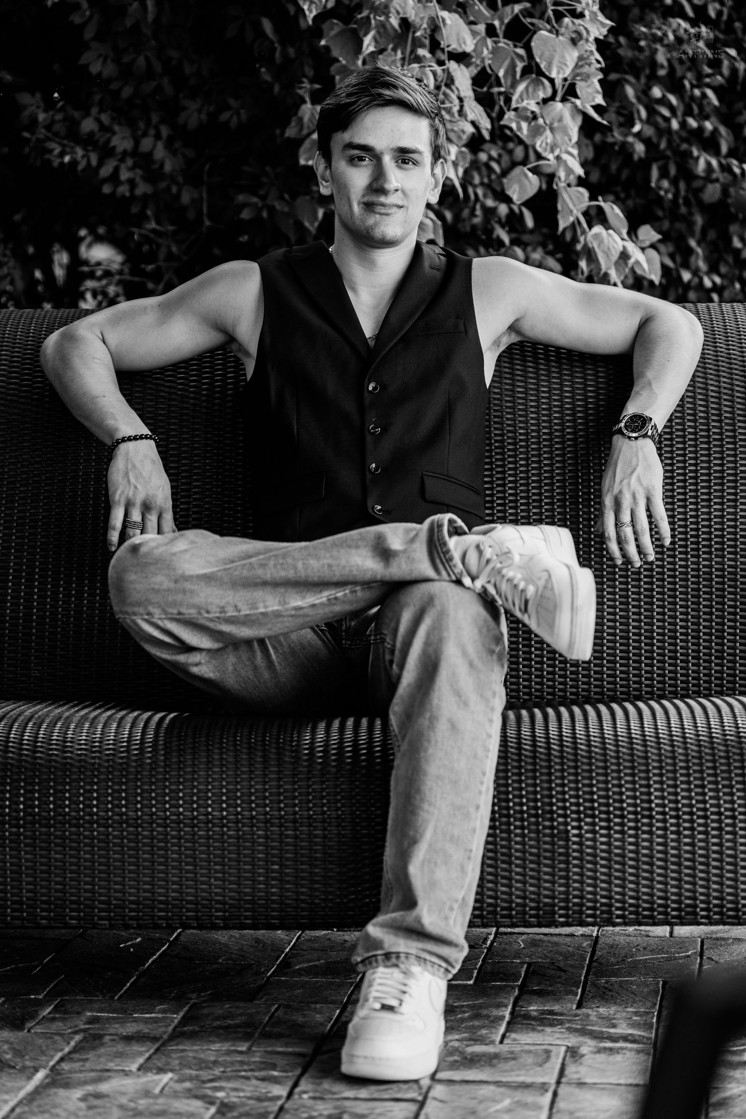 Stylish young man sitting confidently on outdoor wicker sofa in black and white portrait.