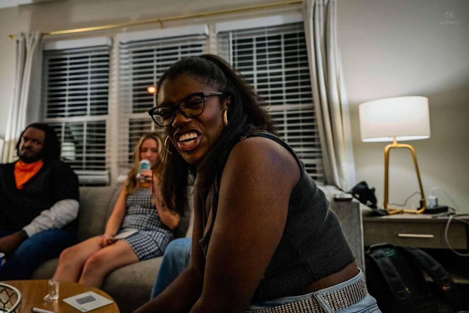 Laughing young woman with glasses enjoying herself at a cozy indoor house gathering.