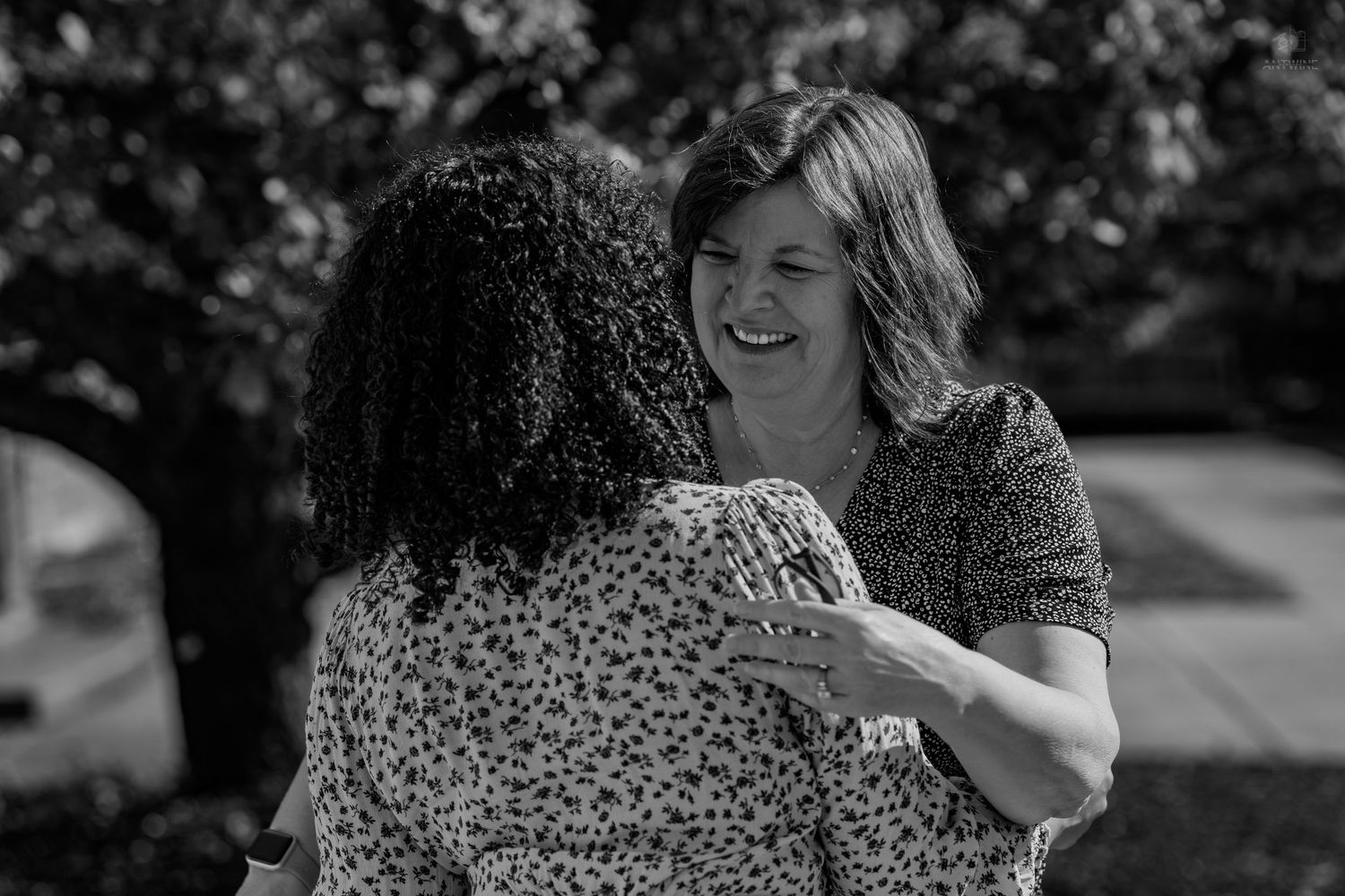 Black and white photo of two women smiling and embracing warmly outdoors.