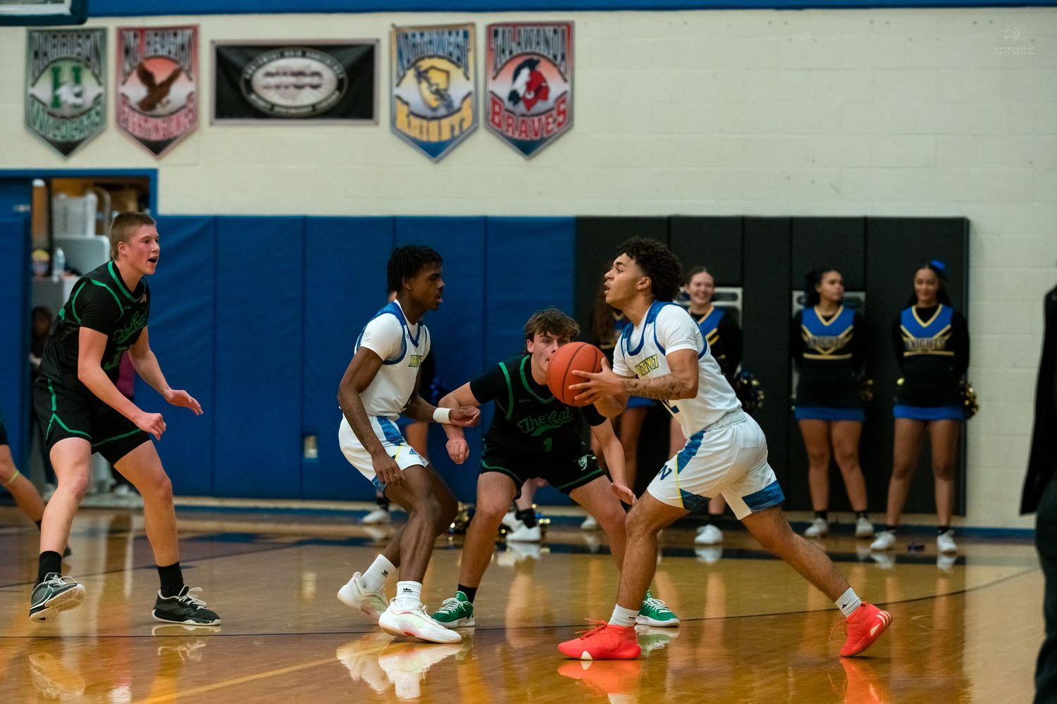 Blue-uniformed player drives toward basket while green defenders attempt to block.