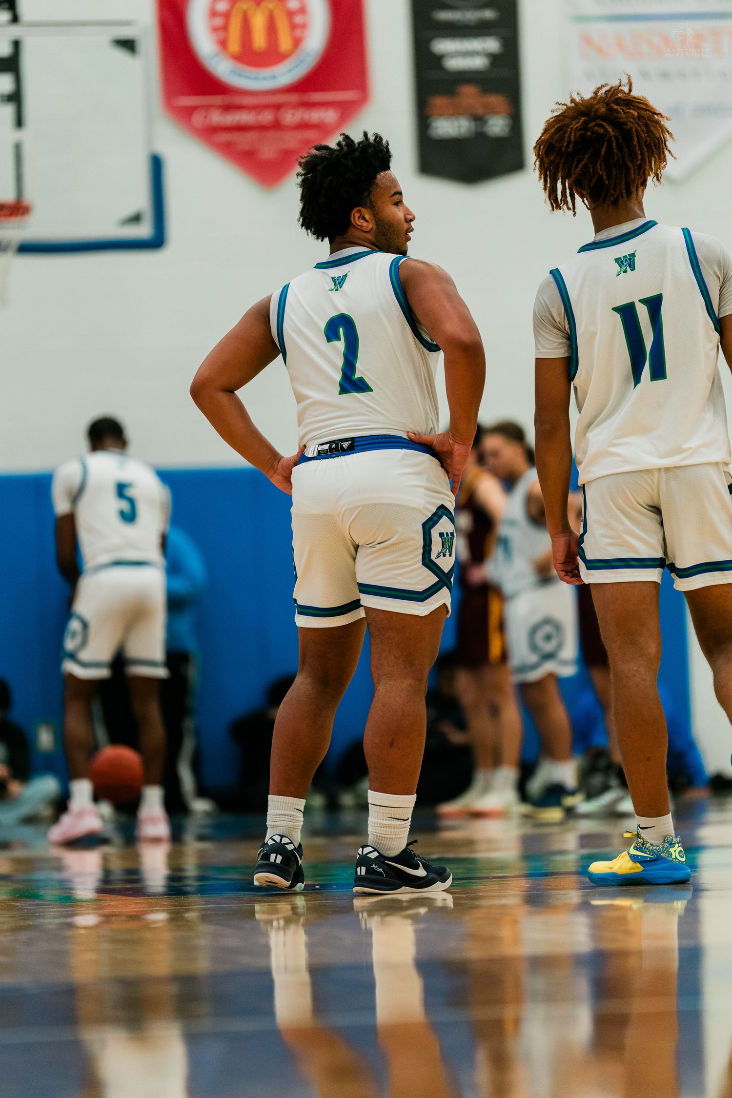 Two Warriors basketball players in white uniforms stand on the court during a game.