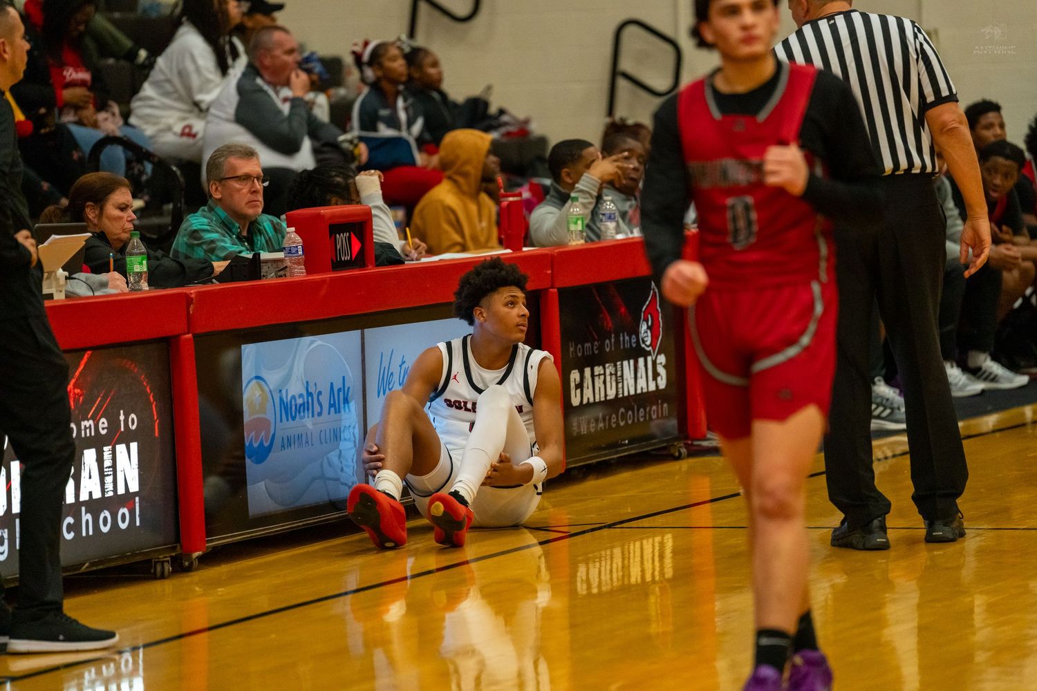 A basketball player sits on the sideline court floor during a Cardinals high school basketball game.