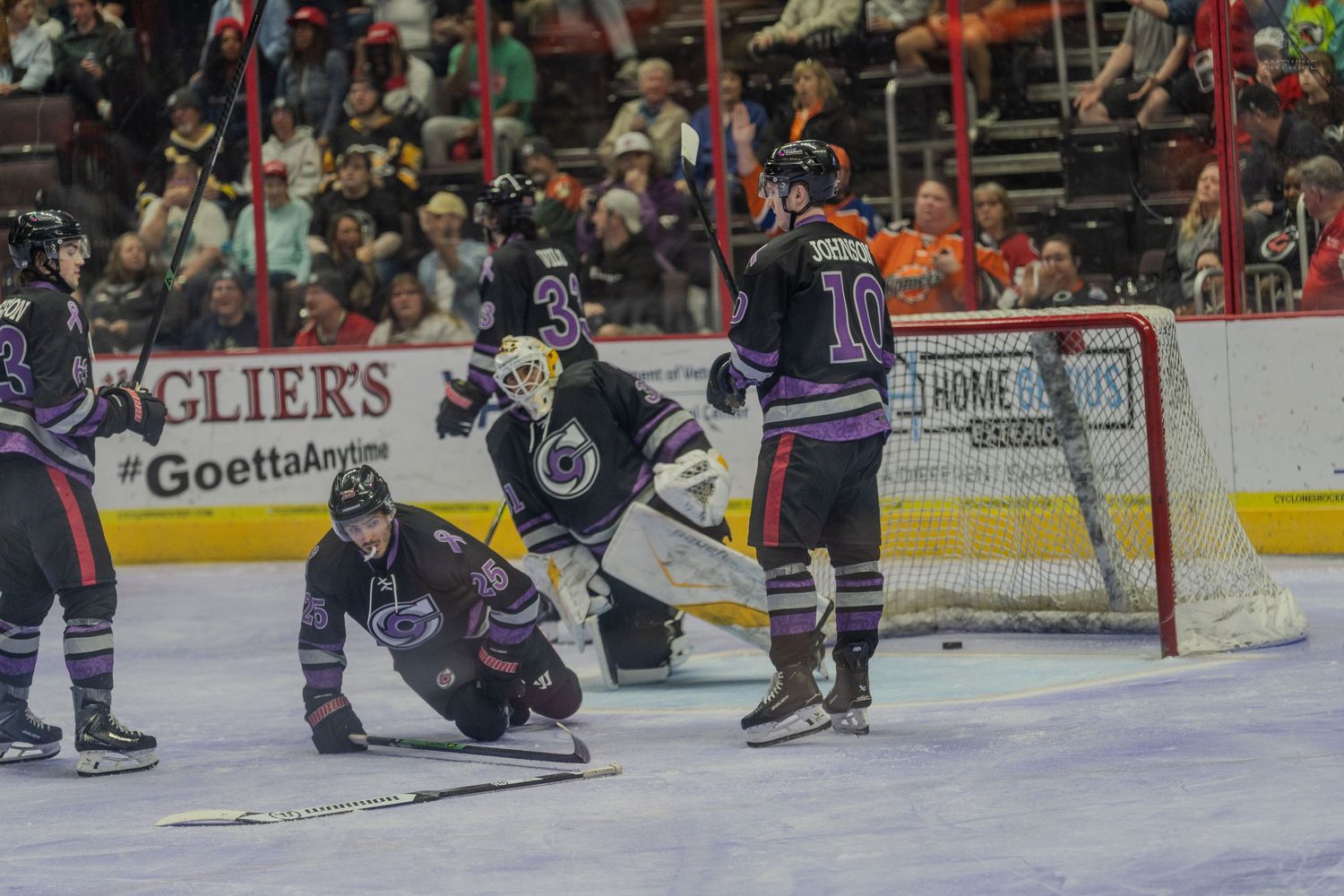 Hockey players react near the goal crease as the puck enters the net during a minor league hockey game.