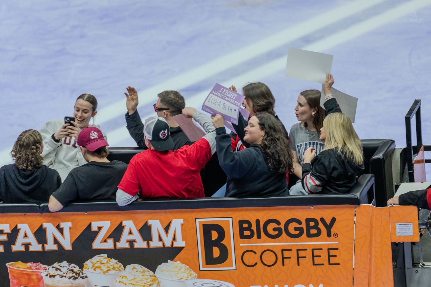 Excited fans cheer in the stands near a Biggby Coffee advertisement at an indoor hockey arena.