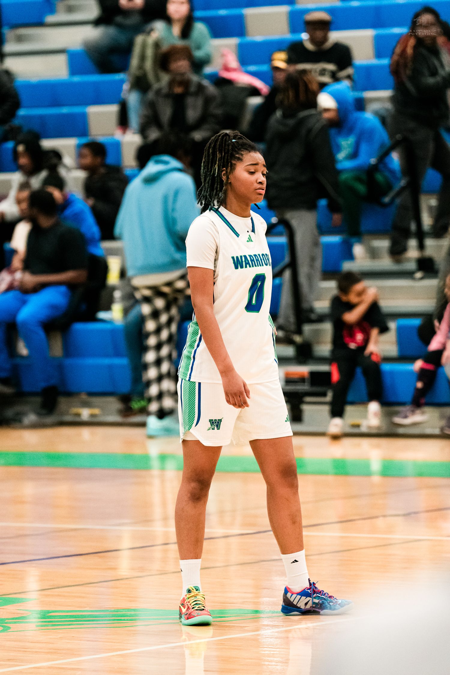 Warriors girls basketball player #0 walks on court in white teal uniform during a high school game.