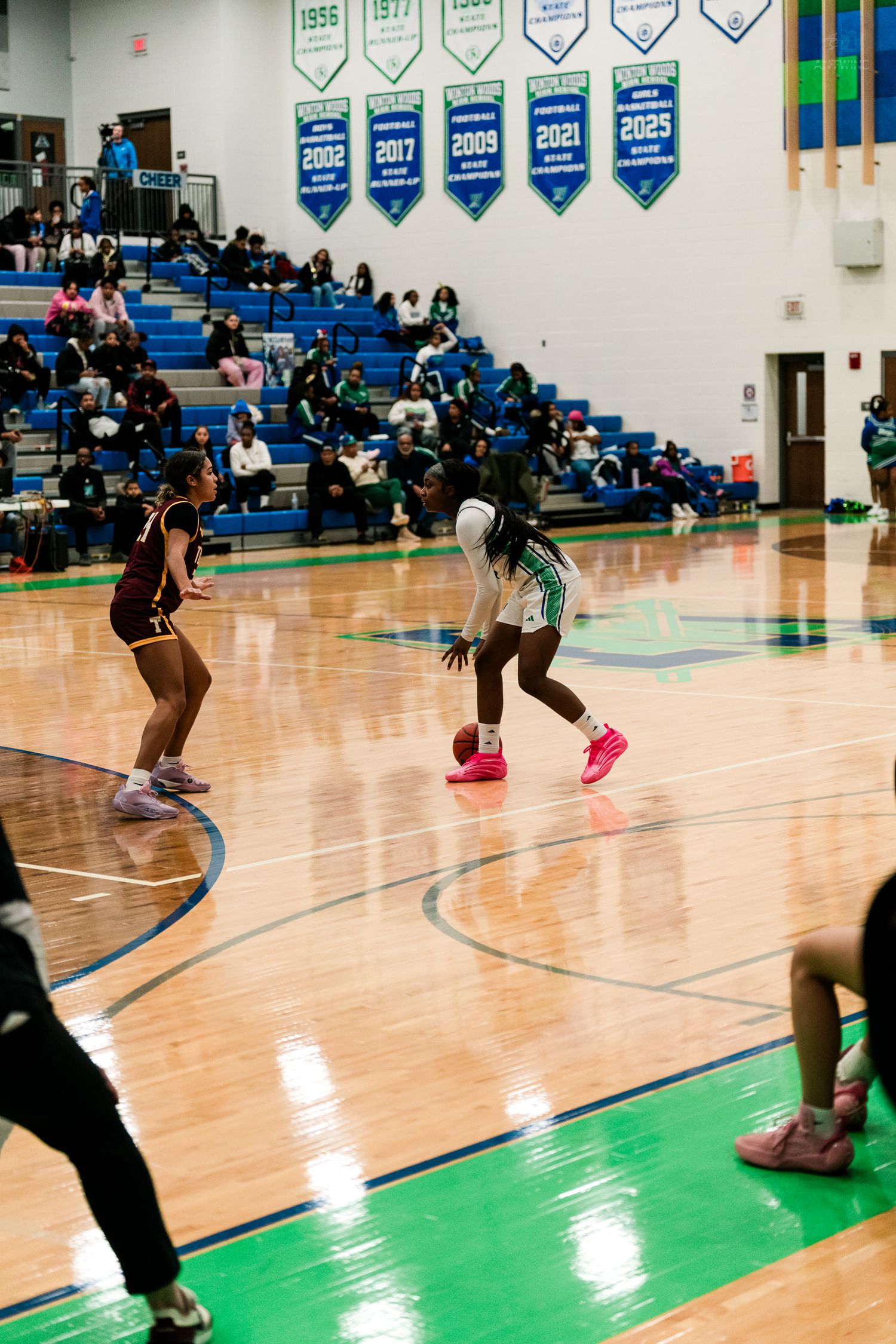 A Warriors girls basketball player in green dribbles the ball at center court during a high school basketball game.