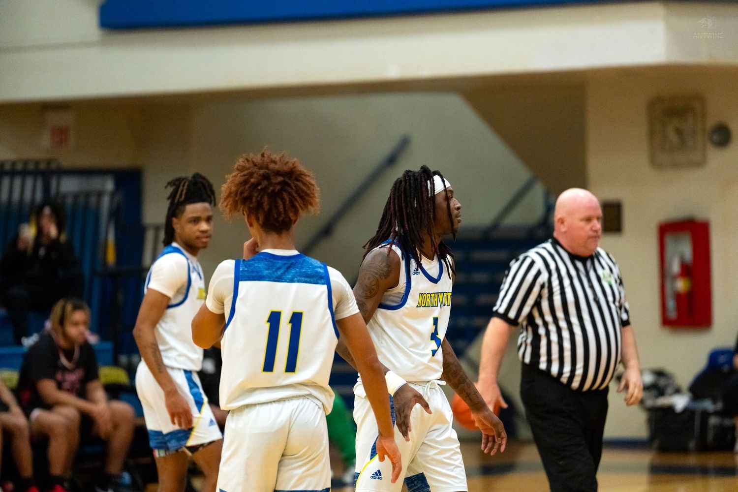 High school basketball players #11 confer near referee during competitive game.