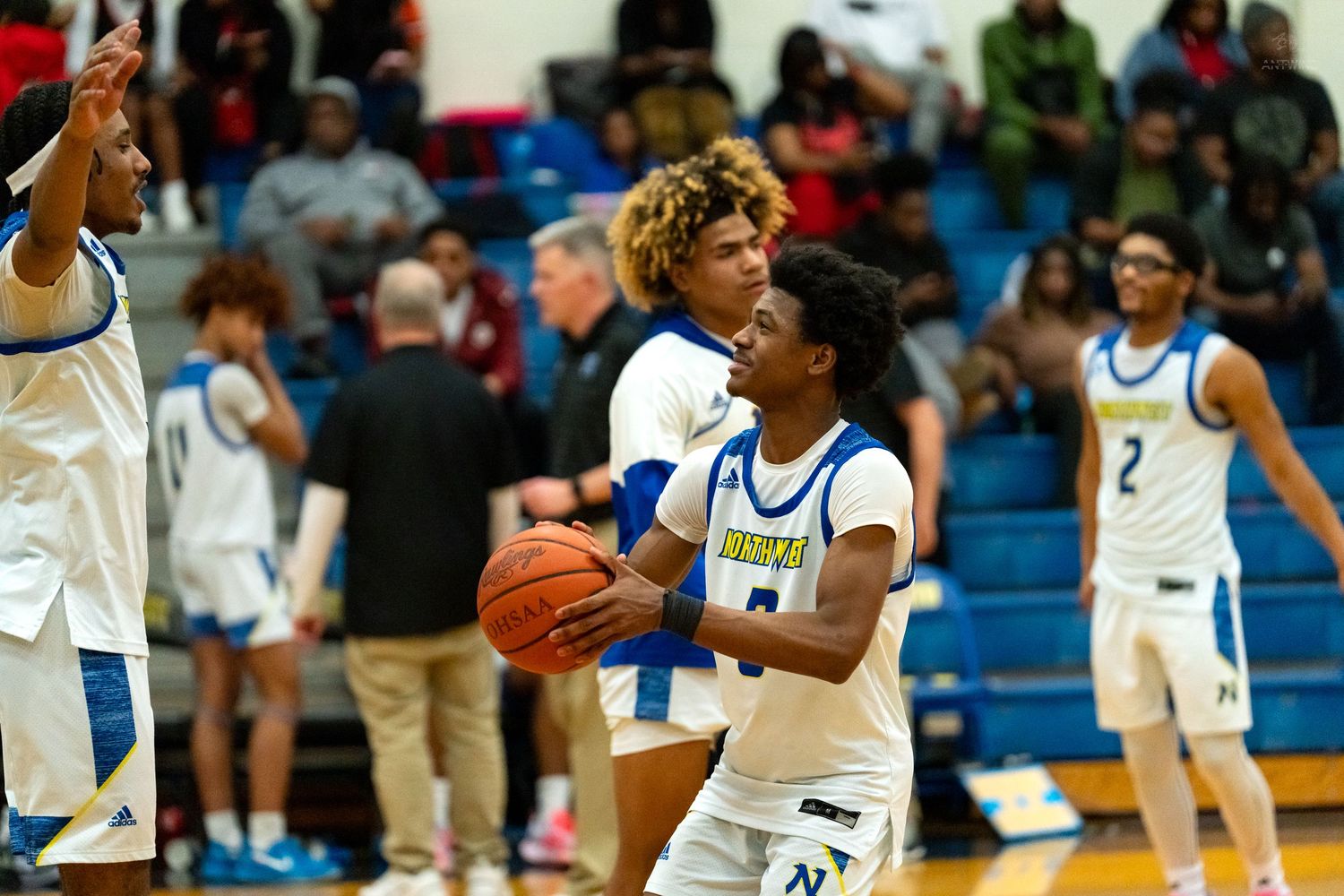 High school basketball players in blue and white uniforms compete for possession during an indoor basketball game.