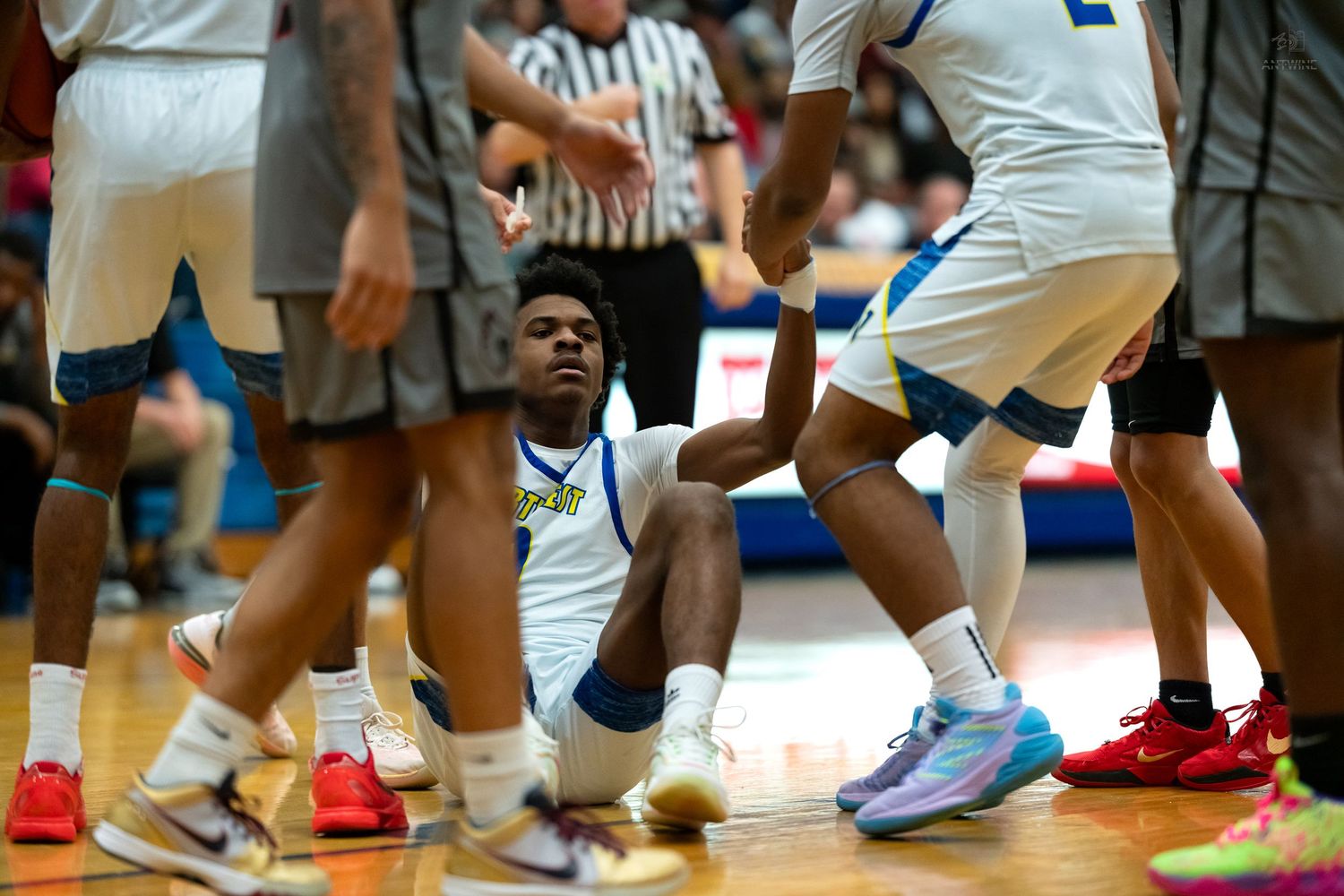 Basketball player in blue and white uniform sits on court floor during timeout.