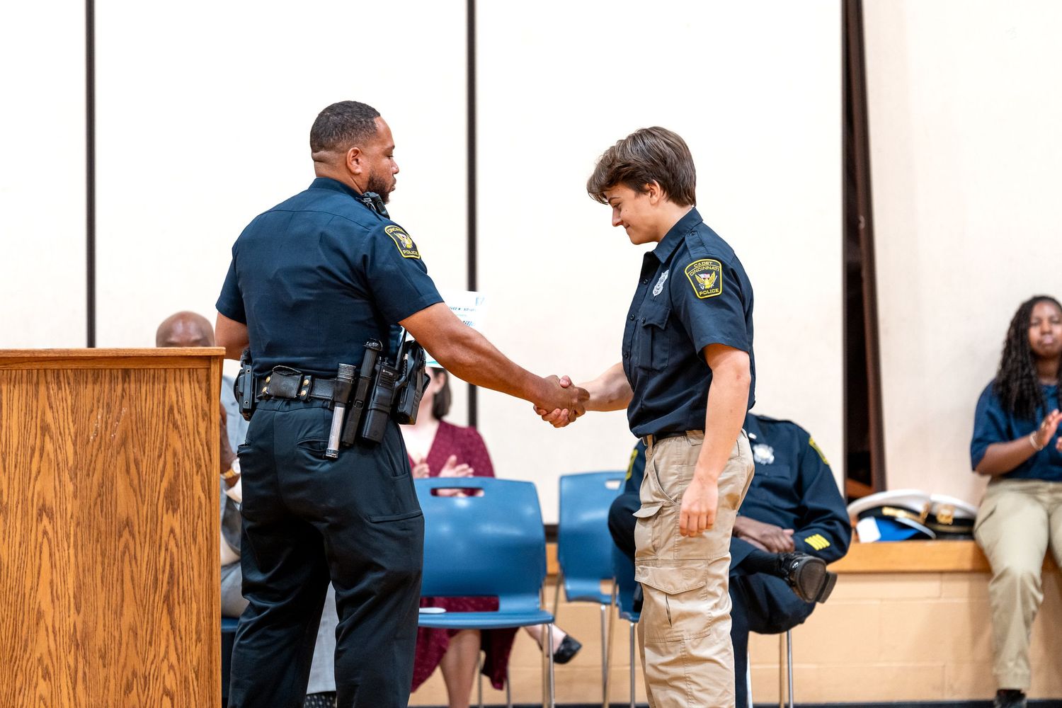 Police officer shaking hands with a young student in uniform during a law enforcement ceremony indoors.