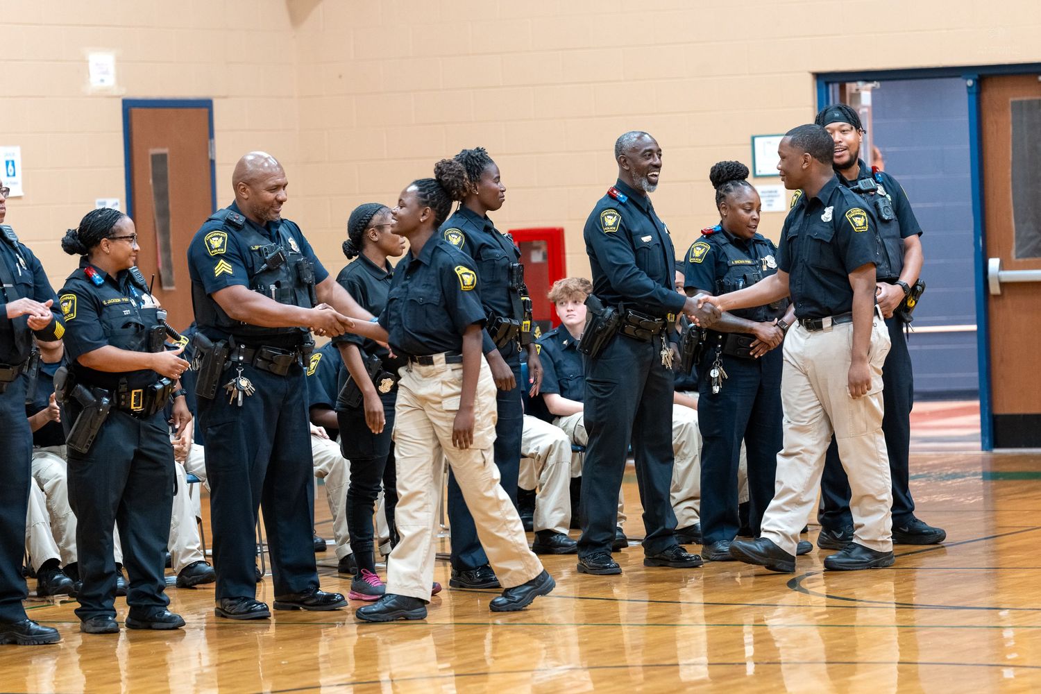 Group of law enforcement officers in uniform standing in a line during an indoor ceremony in a gymnasium.
