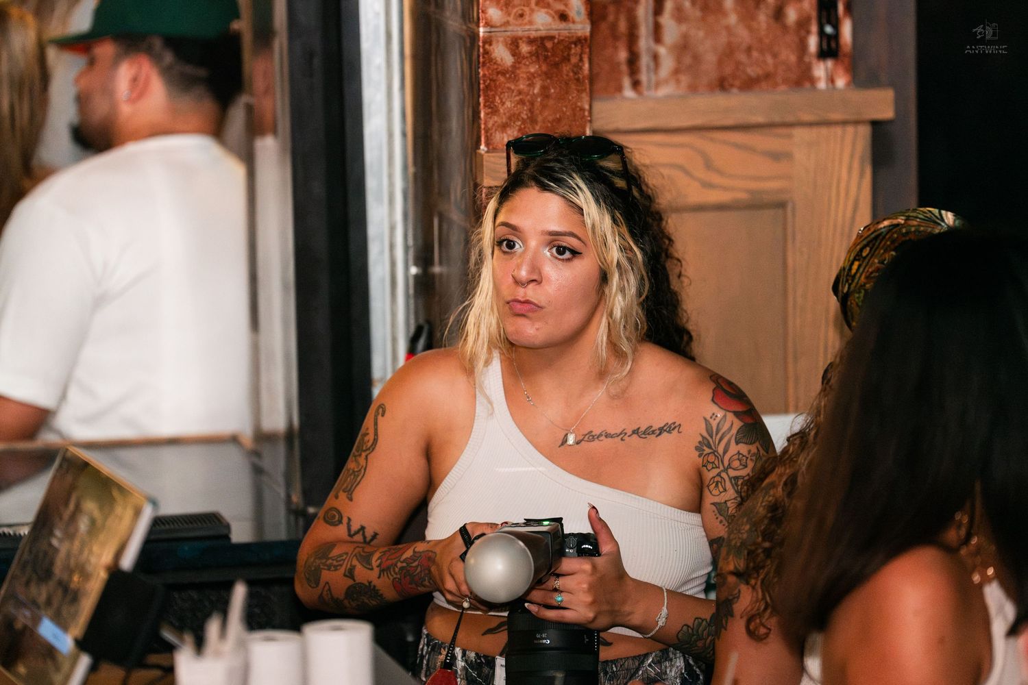 Tattooed woman holding a camera at a casual indoor social event.