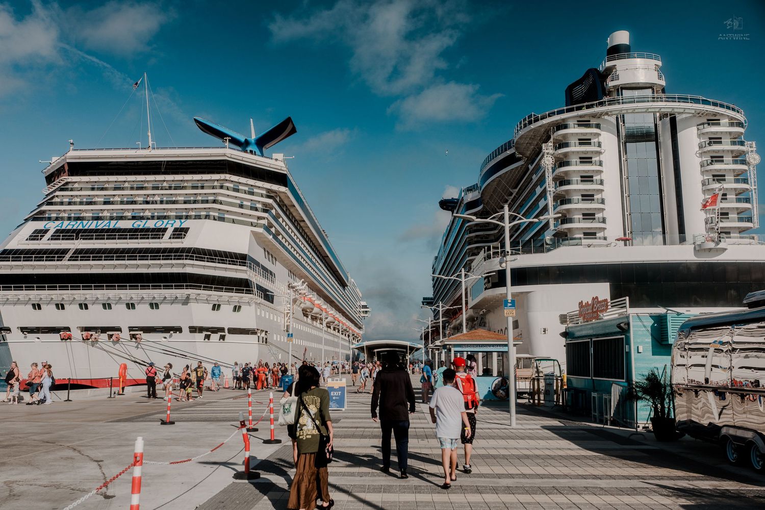 Two large cruise ships docked at a busy port terminal with passengers walking along the pier.