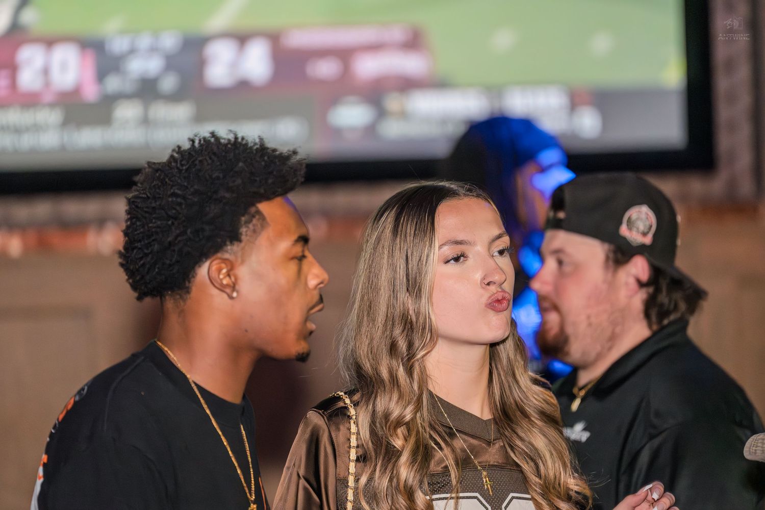 Young man and woman posing together at a sports bar with a game on TV.