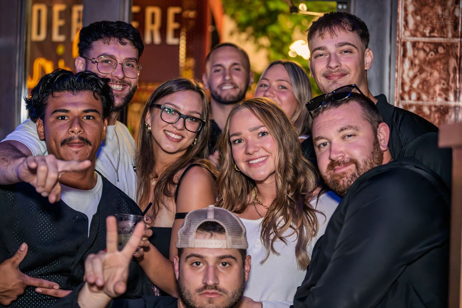 Large group of young friends posing together for a fun nightlife photo outside a bar.