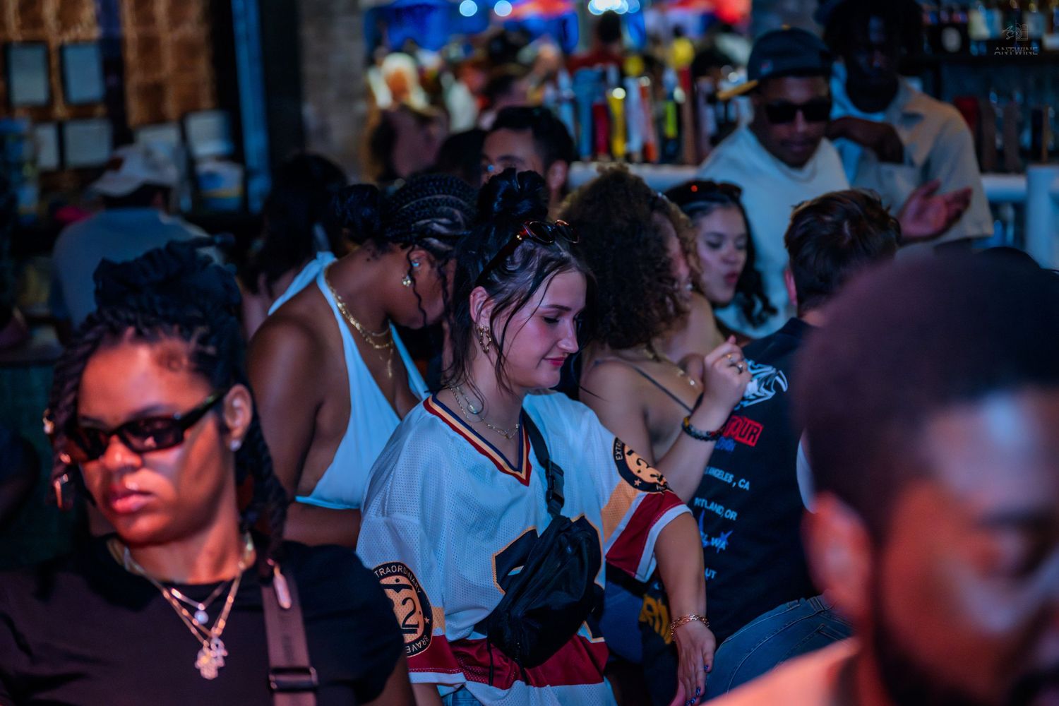 Diverse crowd of young people enjoying a busy nightclub, with colorful lighting and music.