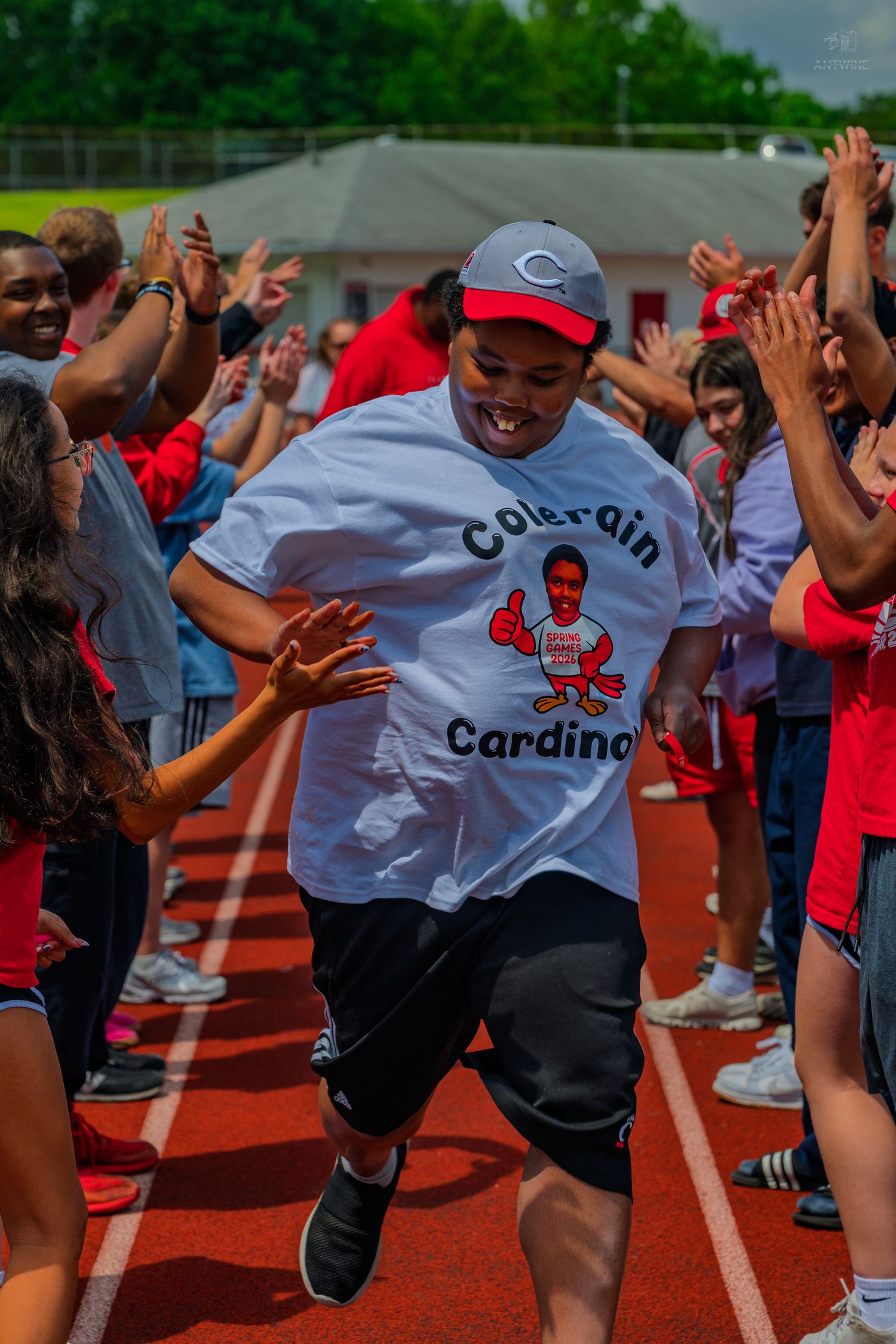 Student in Colerain Cardinals shirt runs through cheering crowd on red track at school sports event.