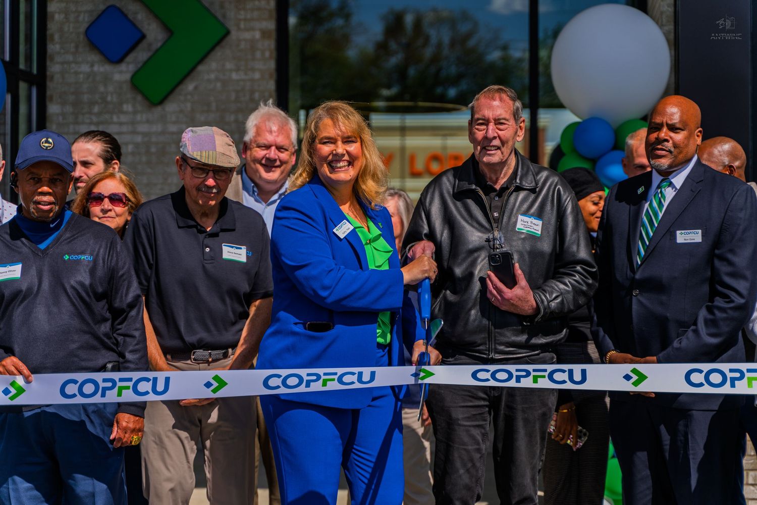 COPFCU credit union ribbon cutting ceremony with smiling staff and officials celebrating a grand opening outdoors.