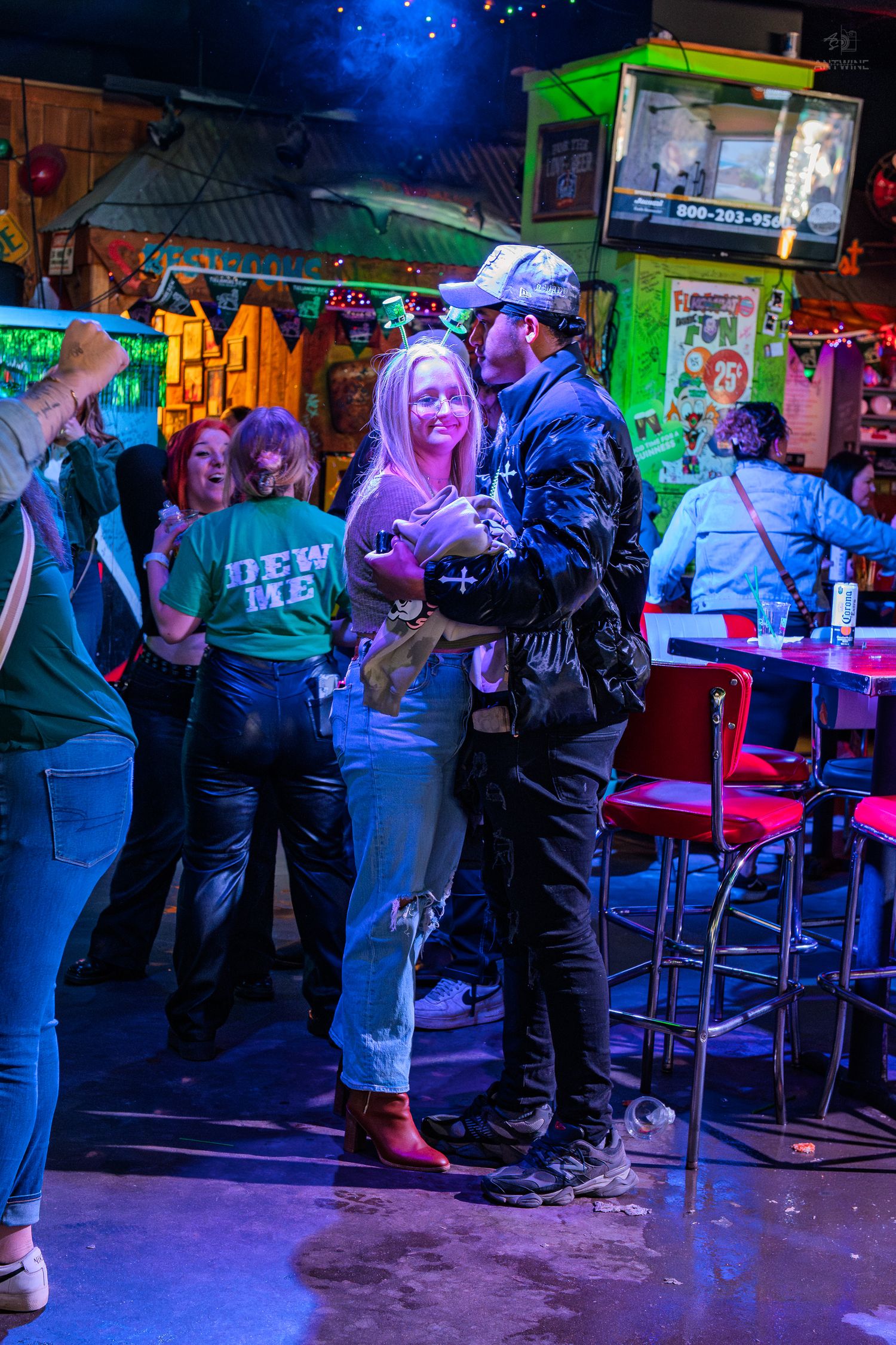 Couple dancing together in a lively, colorful bar with neon lights and other patrons in the background.