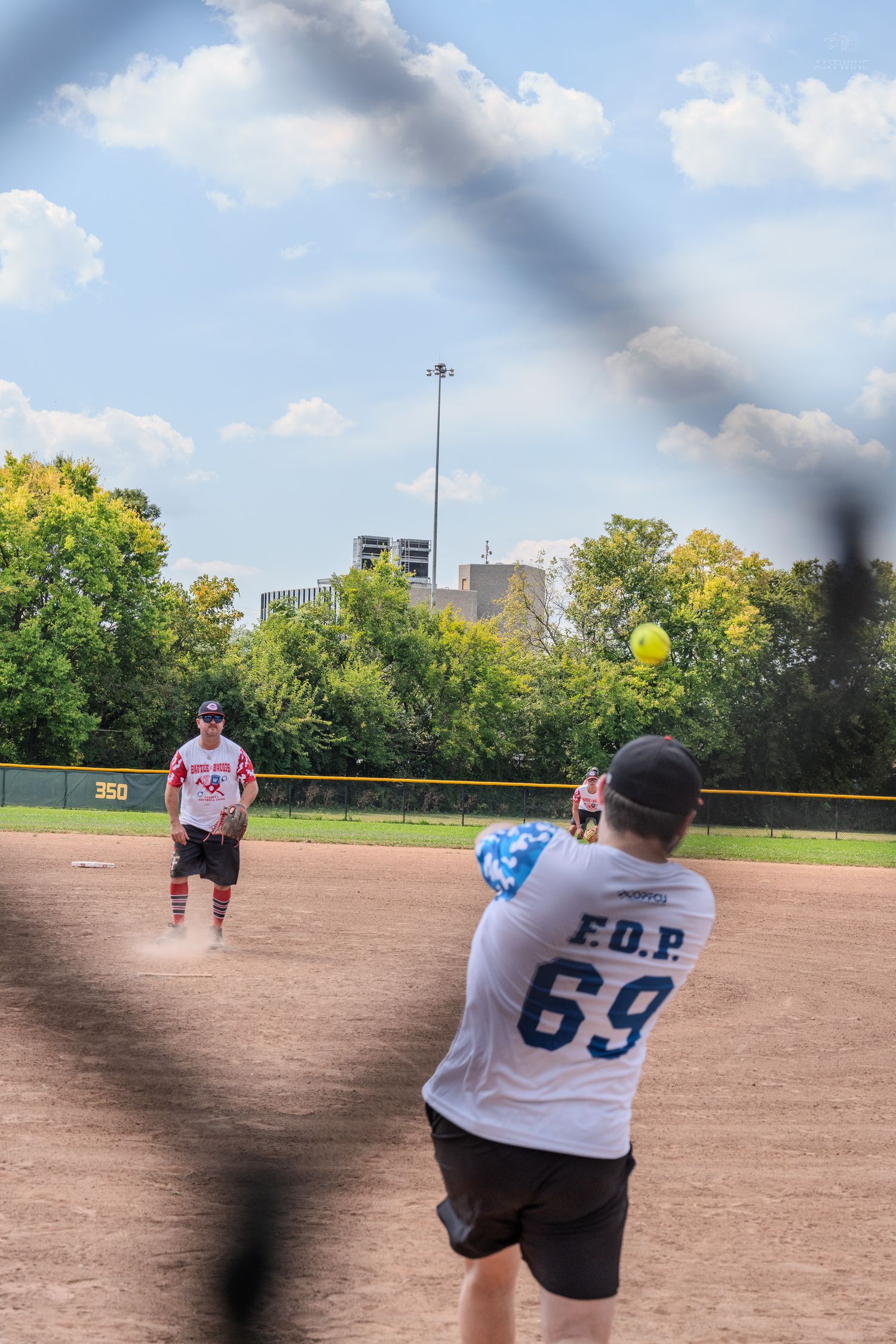 Player in FOP 69 jersey pitches yellow softball on sunny outdoor diamond.