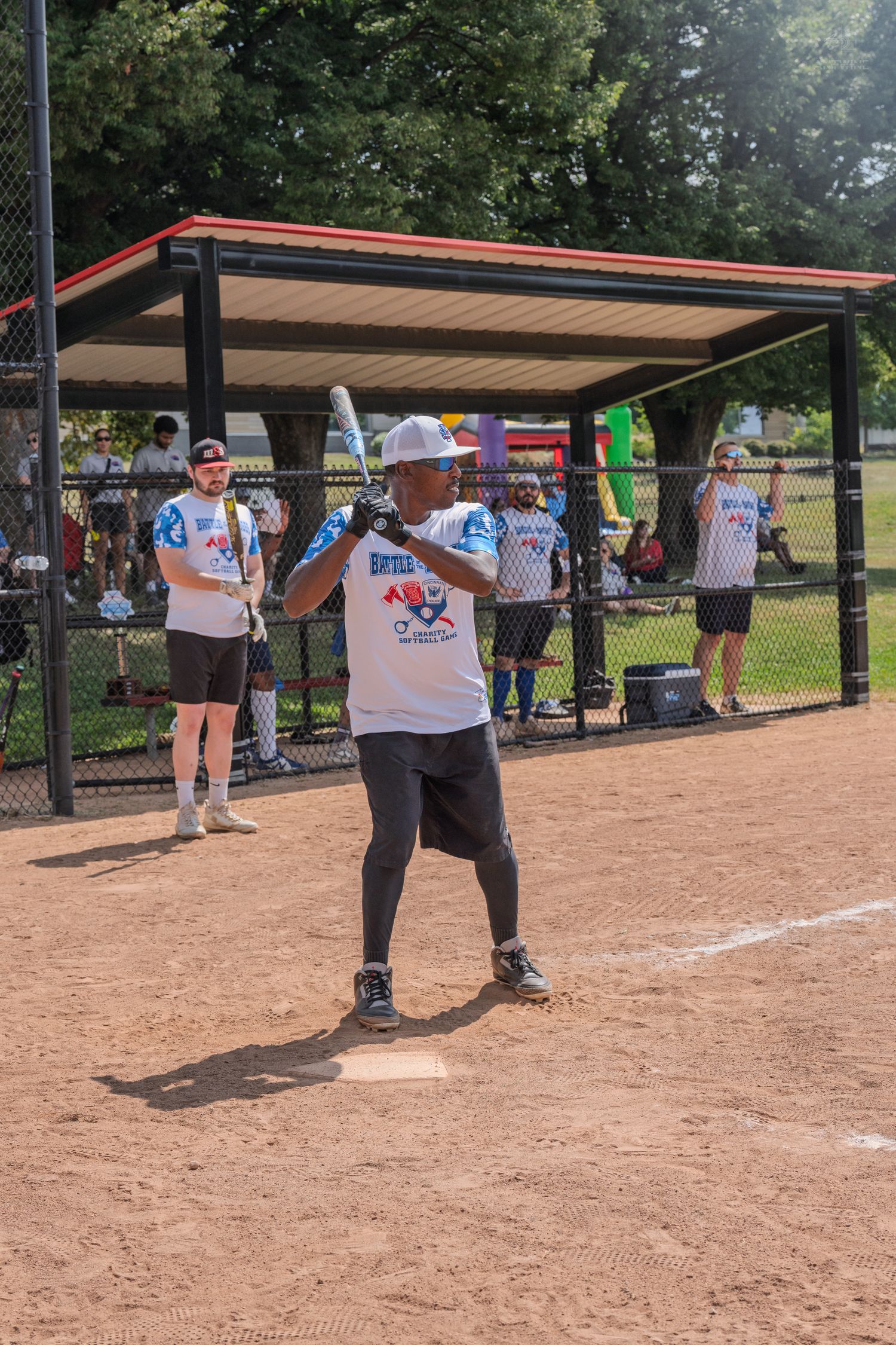 Softball player in white jersey at home plate preparing to bat during charity Battle of the Badges game.
