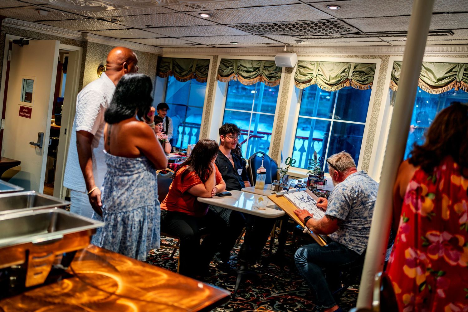 Guests dining and socializing in an elegant cruise ship restaurant with large windows and warm lighting.