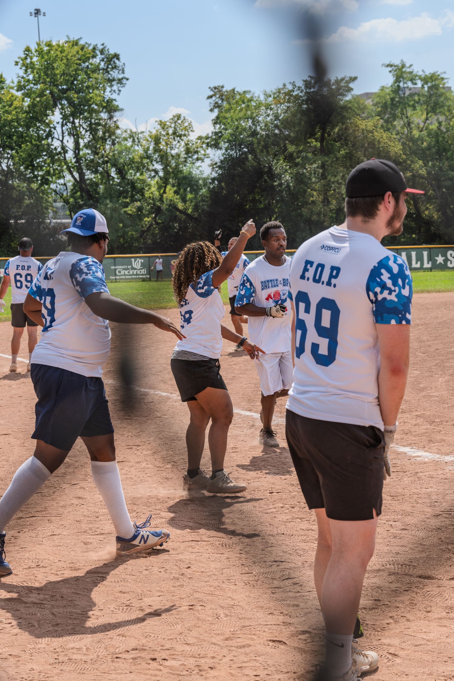 Softball players in FOP jerseys celebrate with high fives on a sunny baseball diamond during a recreational game.