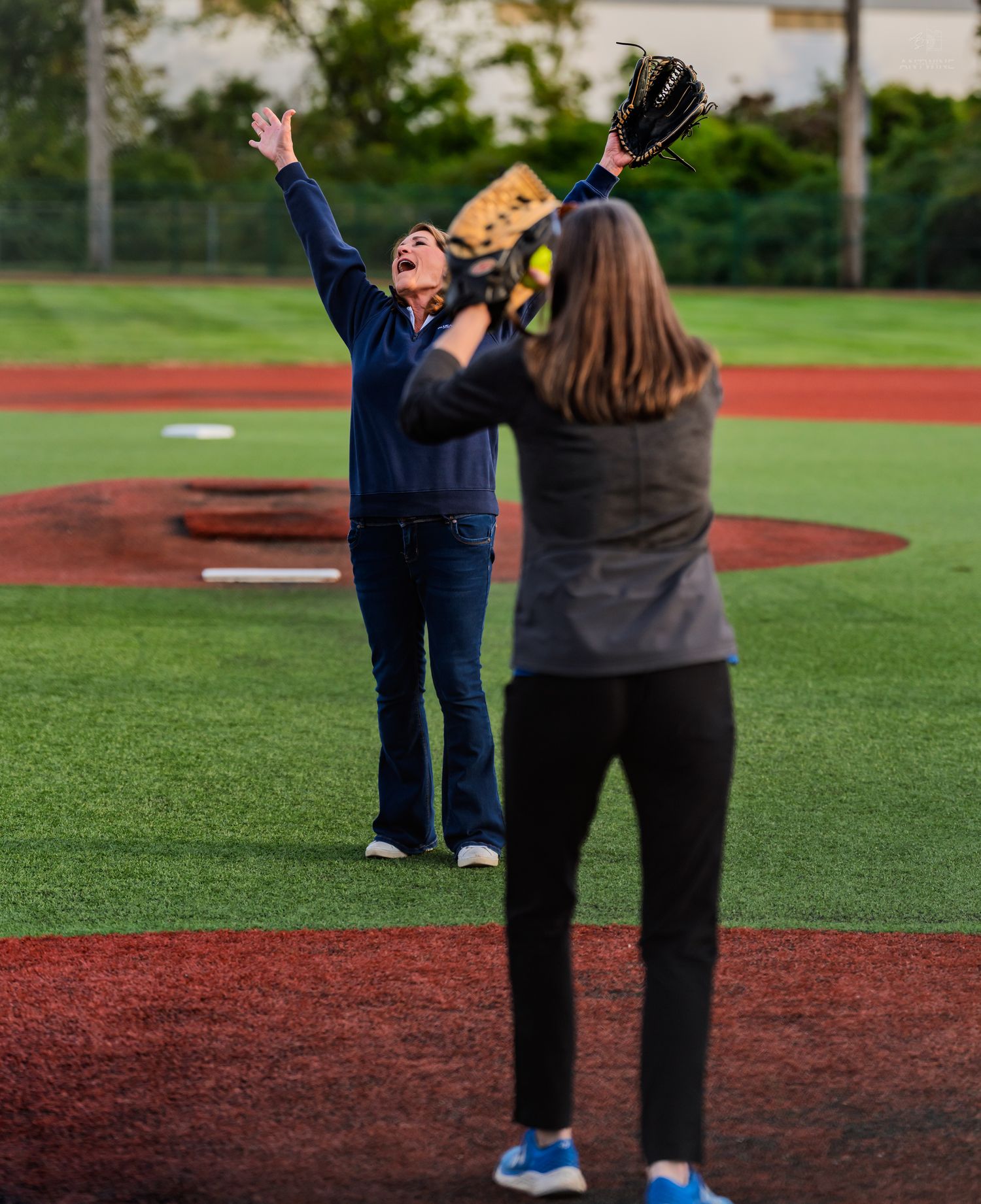 Woman celebrates with arms raised after throwing a softball on a turf baseball field.