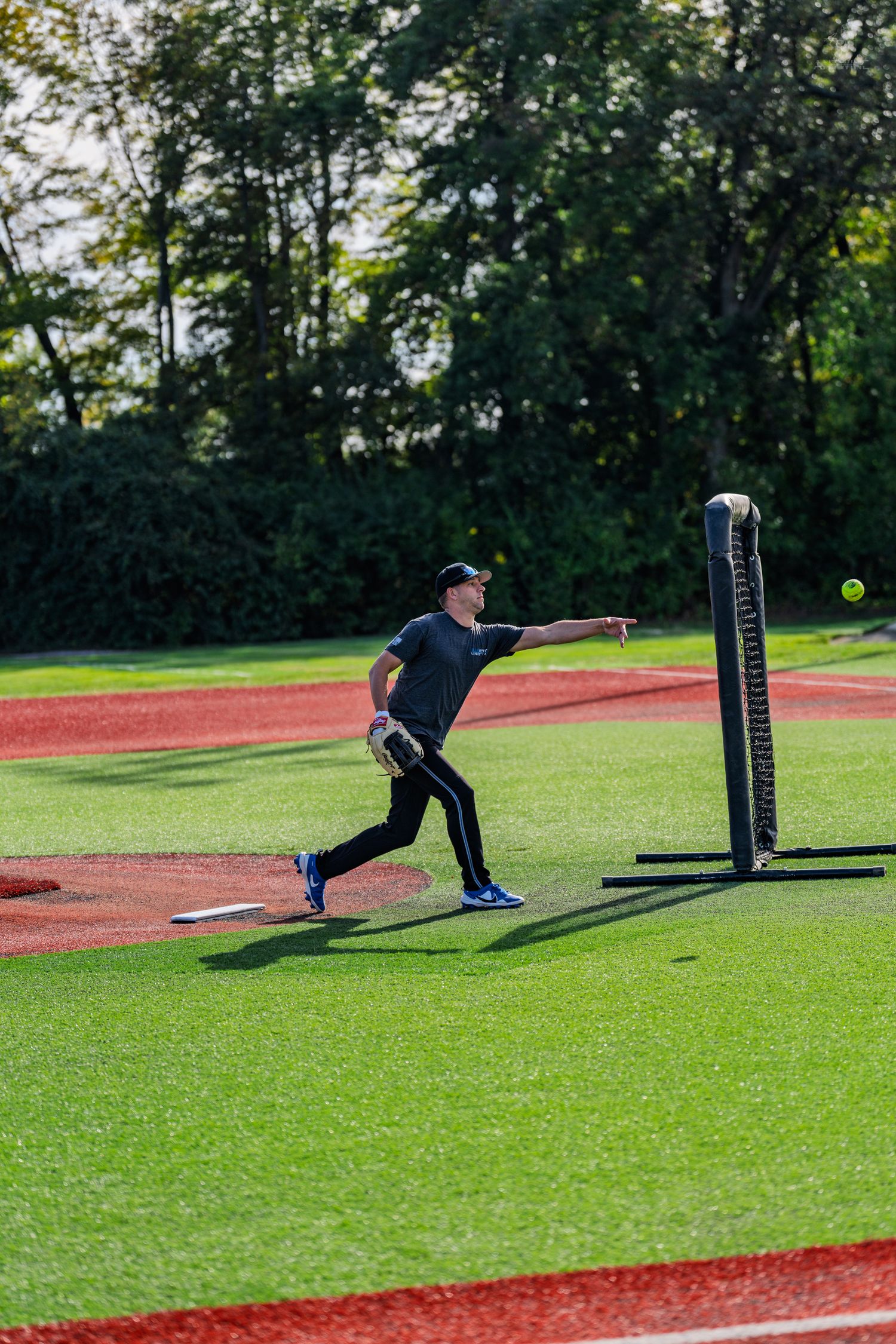 Baseball pitcher throwing ball on green turf field during sunny day practice session outdoors.