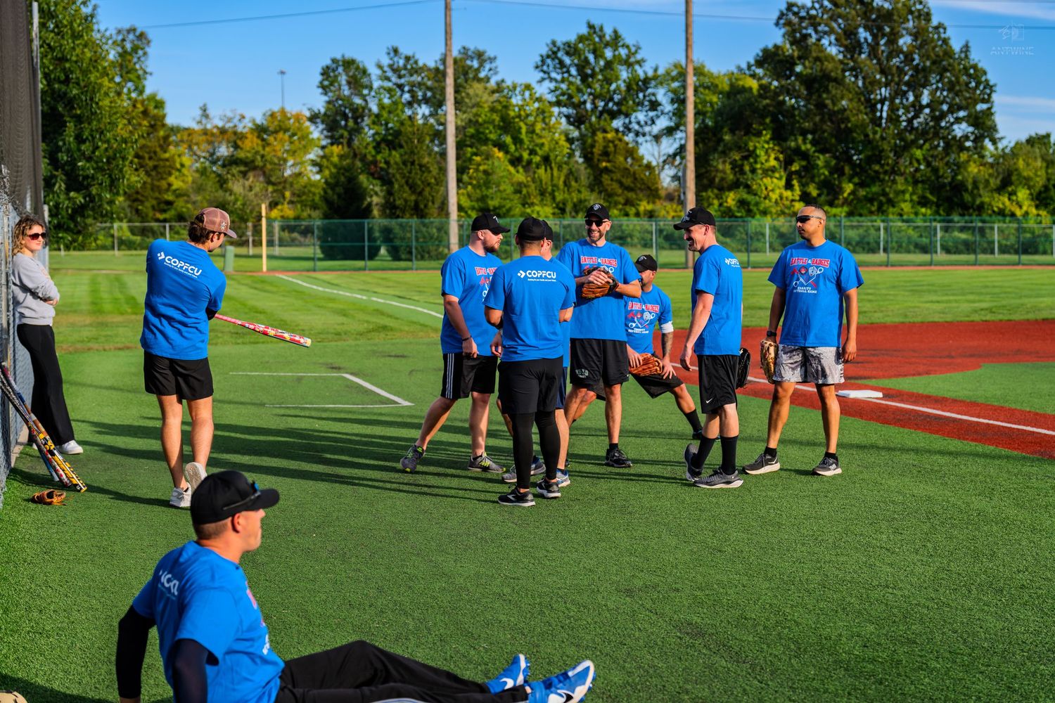 Group of baseball players in blue shirts gathered on green turf field during team practice.