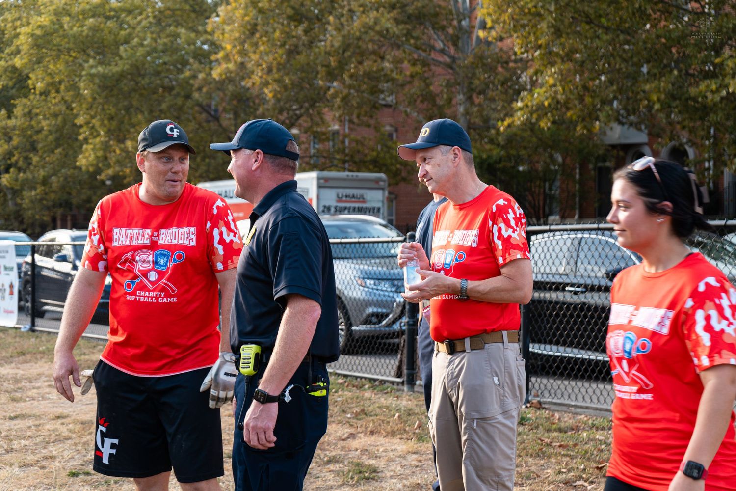 Four softball players in red and black uniforms discuss strategy on an outdoor field during a game.