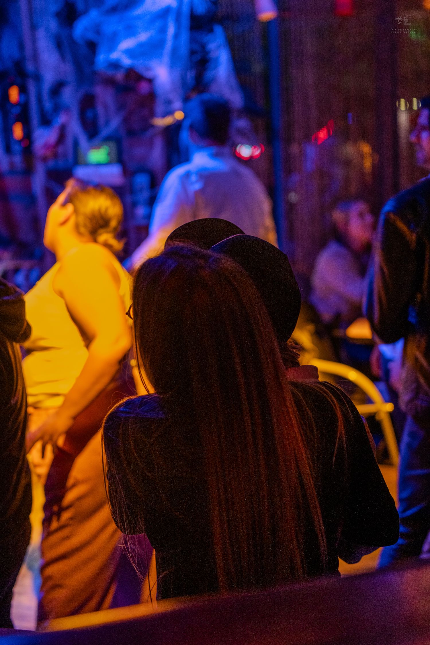 Crowd of people at a dimly lit bar with warm orange and blue neon lighting during a Halloween night event.