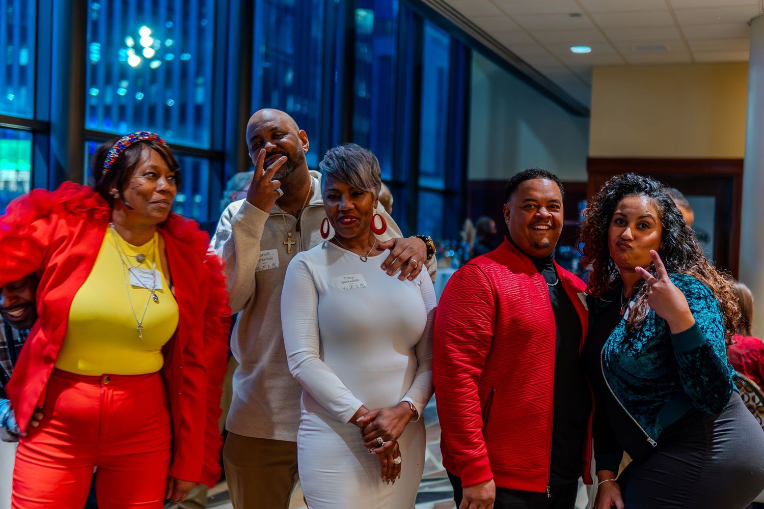 Group of five friends posing together at a formal event, dressed in red, white, and teal outfits.