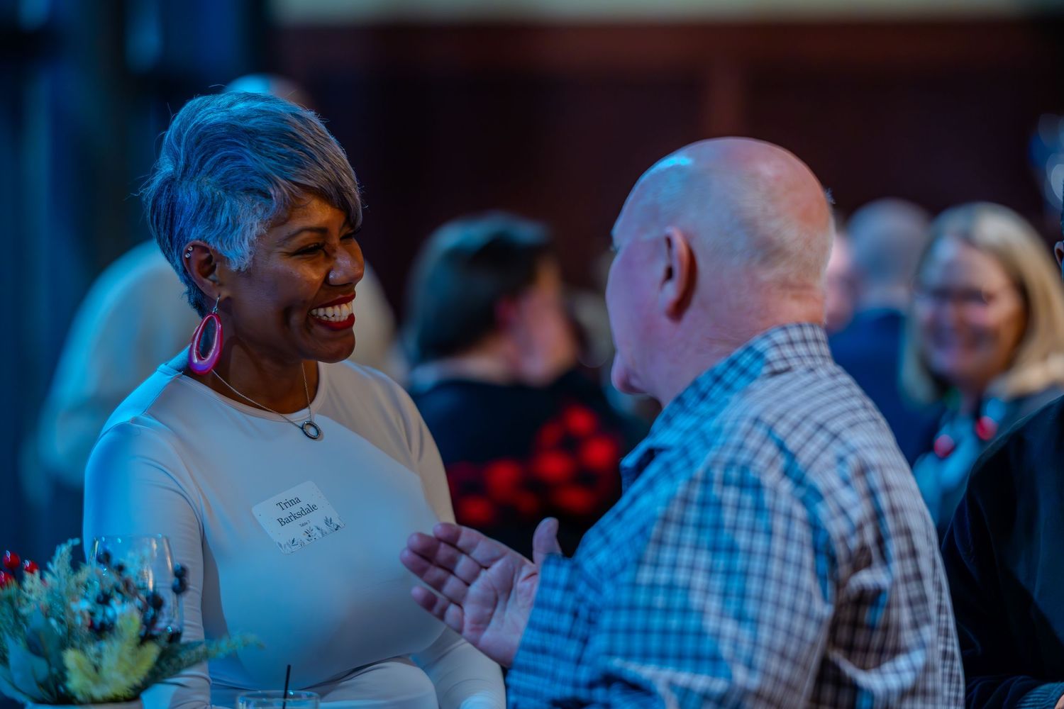 Two people smiling and engaged in conversation at a social networking event in a warmly lit venue.