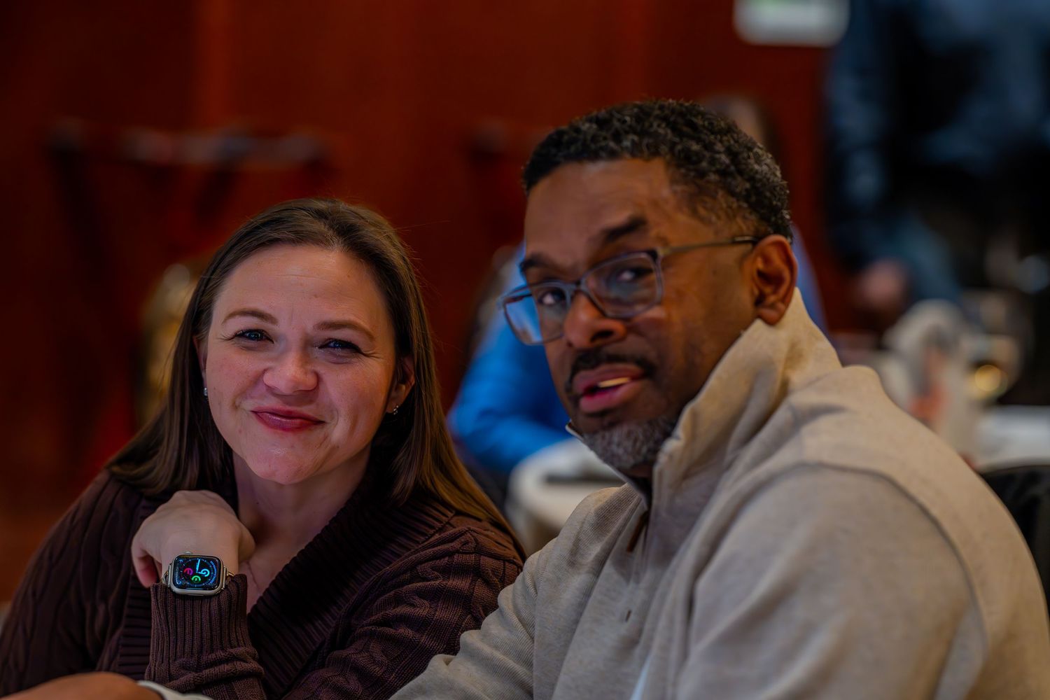 A woman and man sitting together at a table, smiling and engaged in conversation at an indoor event.