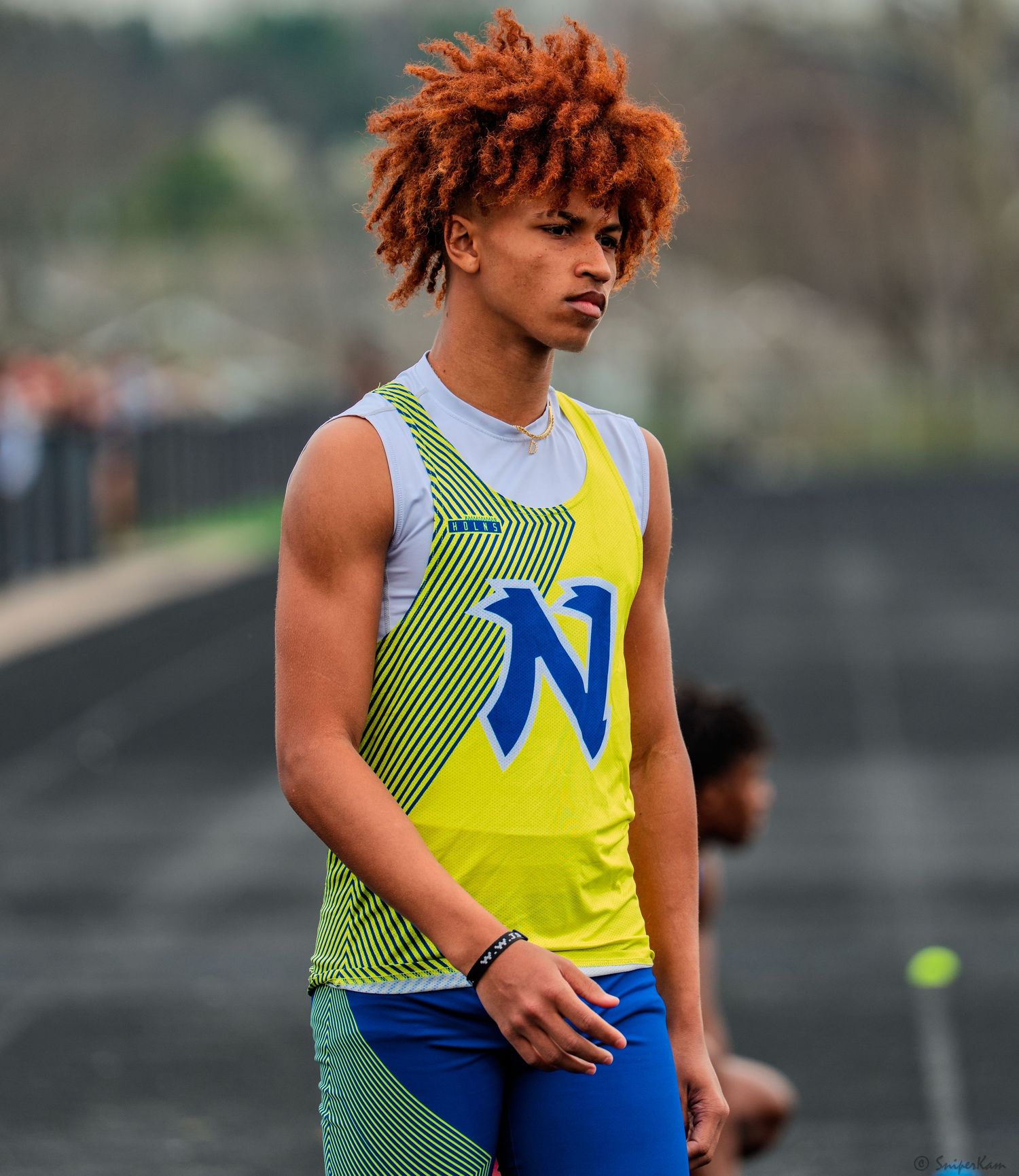 Male high school track athlete with auburn hair wearing yellow and blue N team uniform.