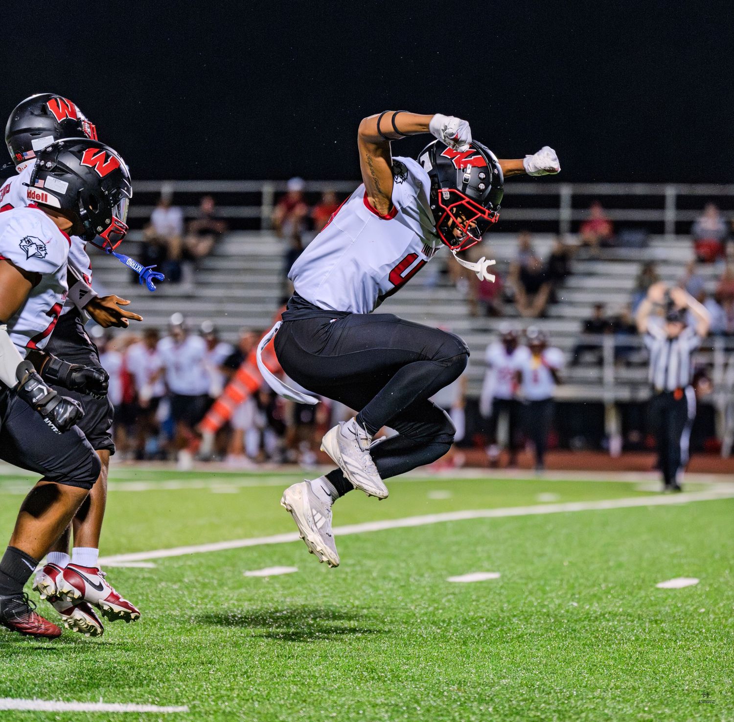 Football player leaping mid-air during night game on green field in red and white uniform.
