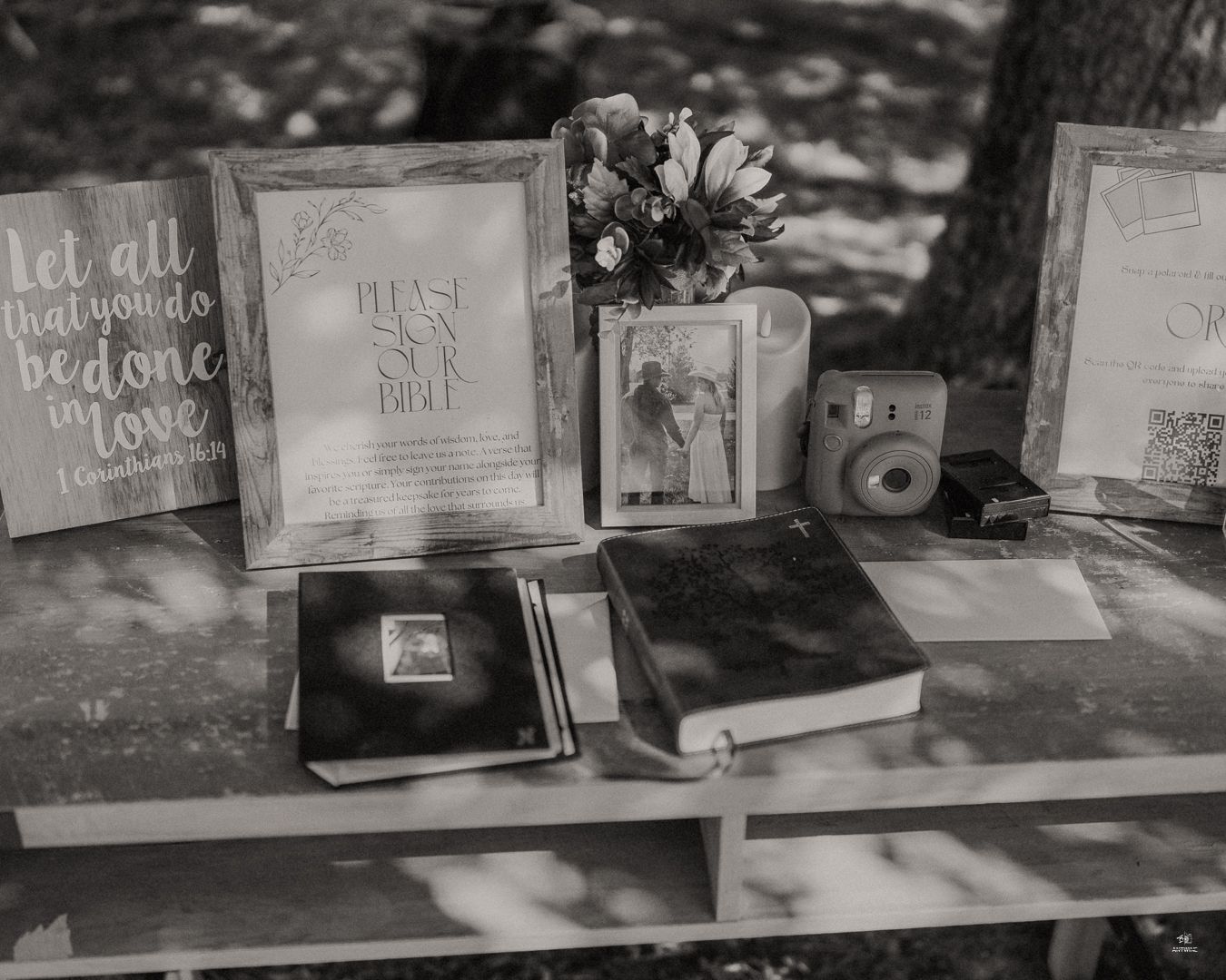 Black and white photo of rustic wedding welcome table with Bible, frames, and Instax camera.