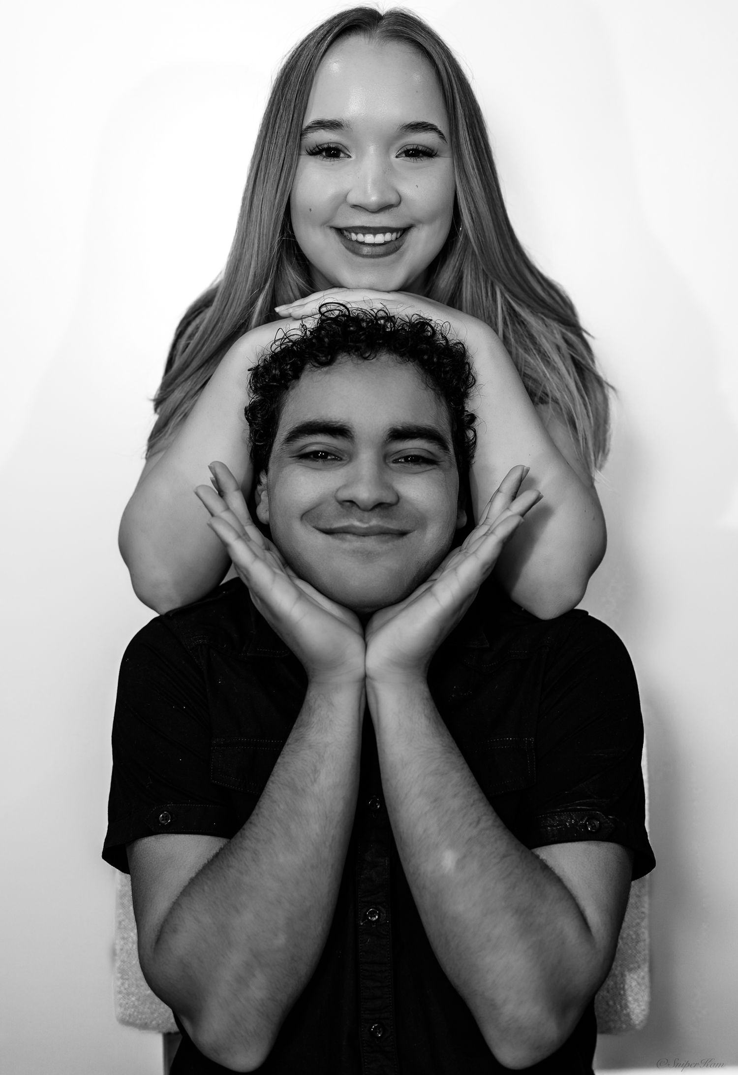 Black and white photo of smiling couple, woman framing mans face with her hands from behind.