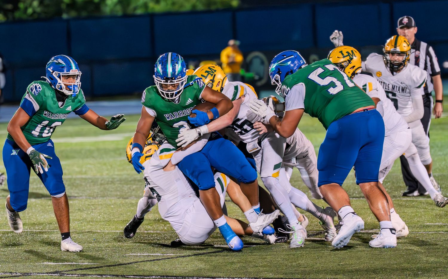 Football players in green and gold uniforms battle for yards during a high school game.