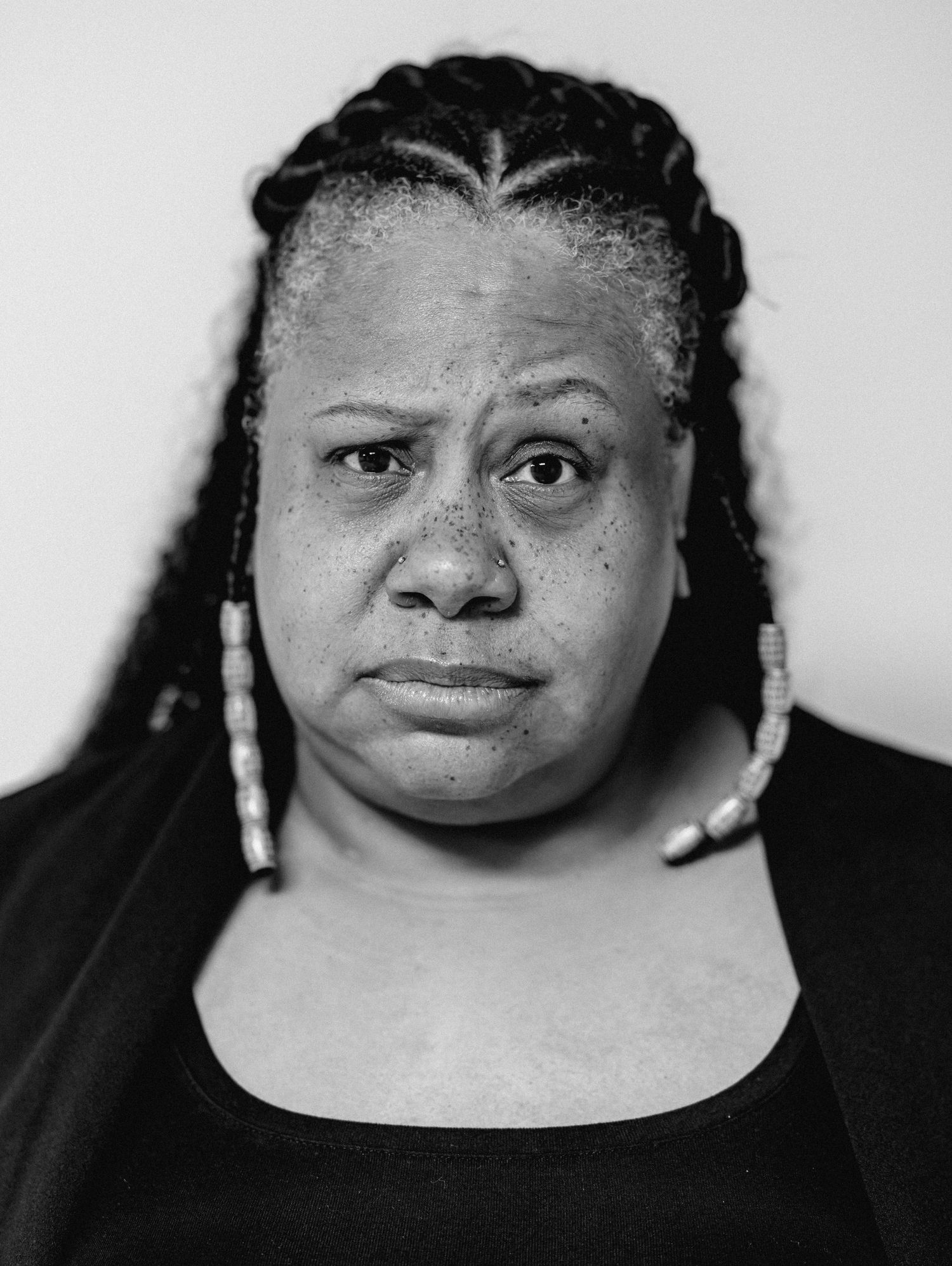 Black and white portrait of a woman with braided hair and bead earrings with a serious expression.
