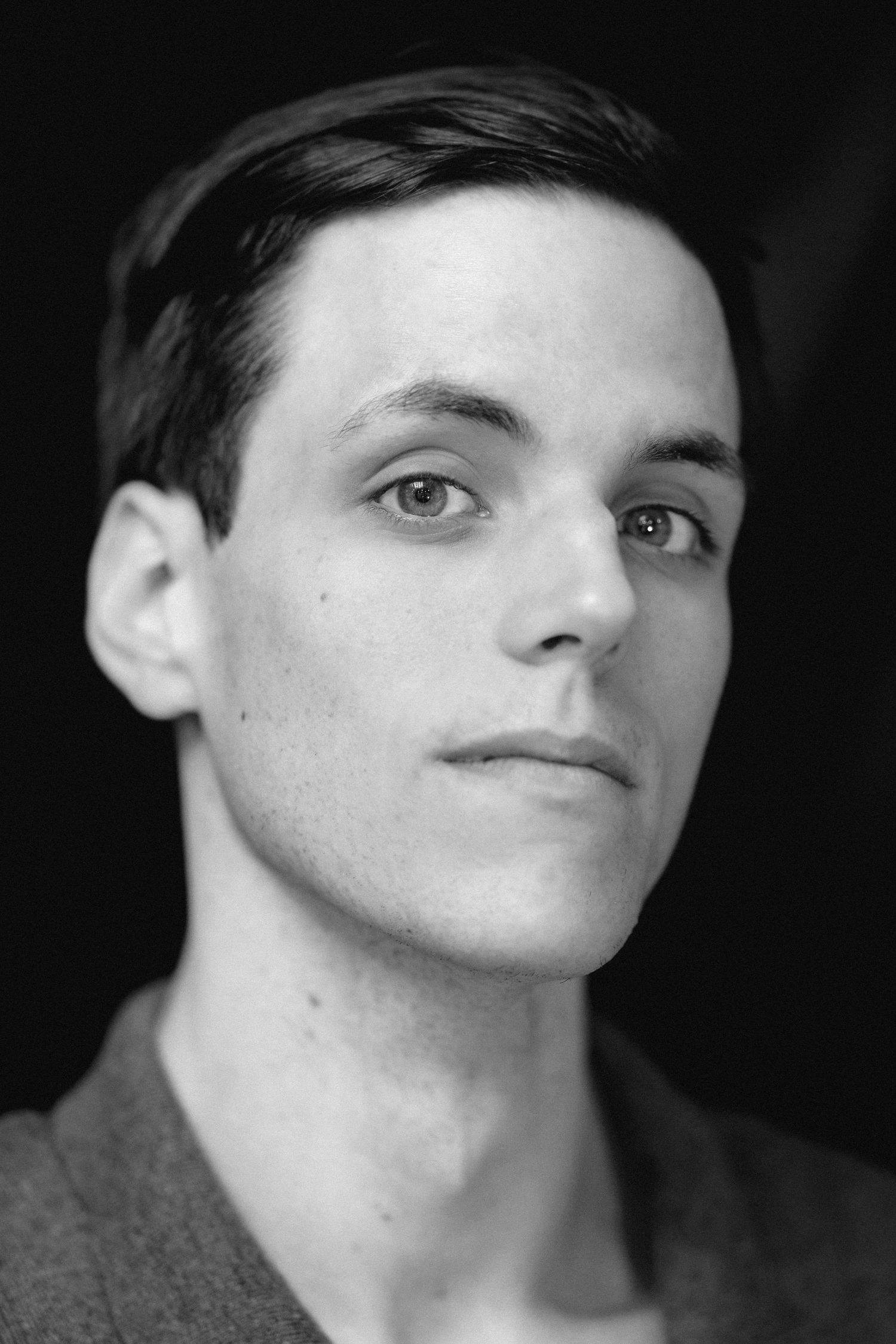 Black and white professional headshot of a young man with short dark hair wearing a gray shirt.
