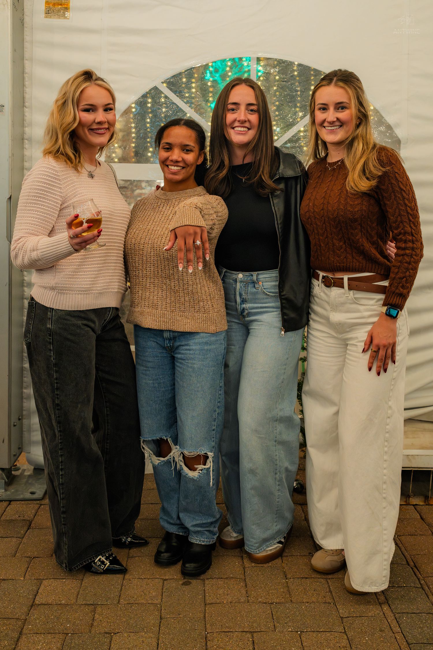 Four young women posing together inside a white tent, one showing off an engagement ring.