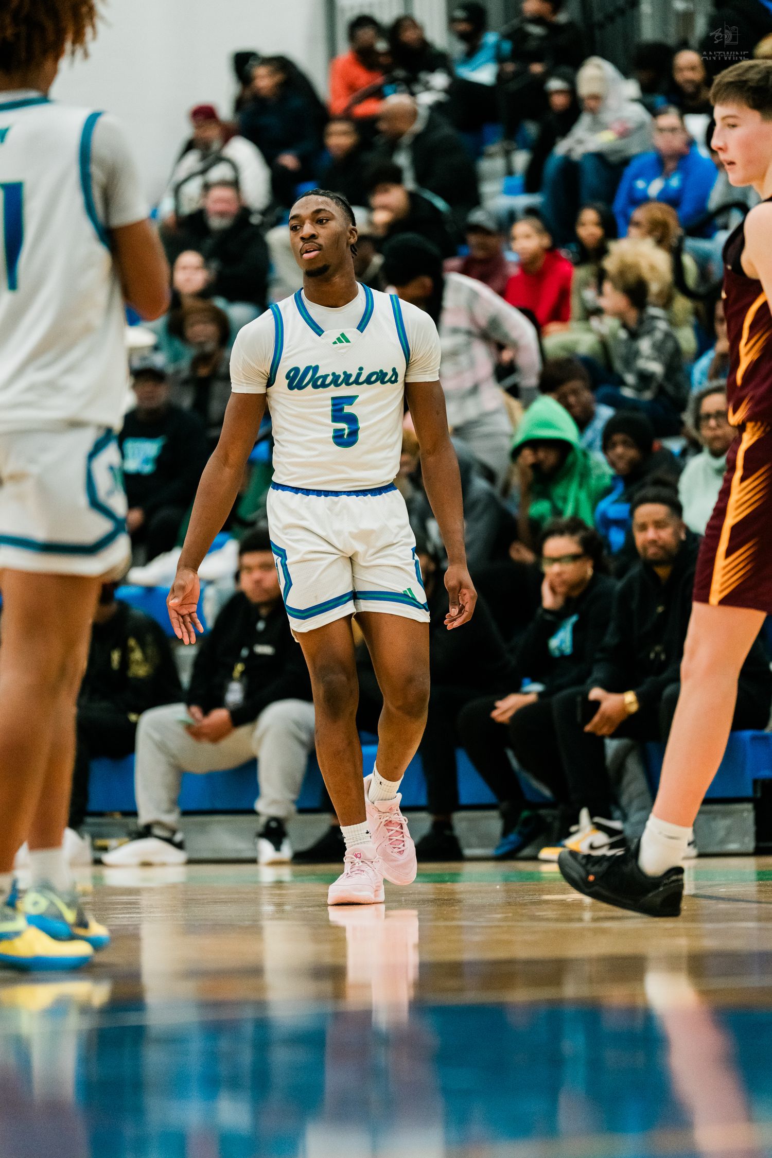 Warriors basketball player number 5 in white uniform walks confidently on a reflective hardwood court.