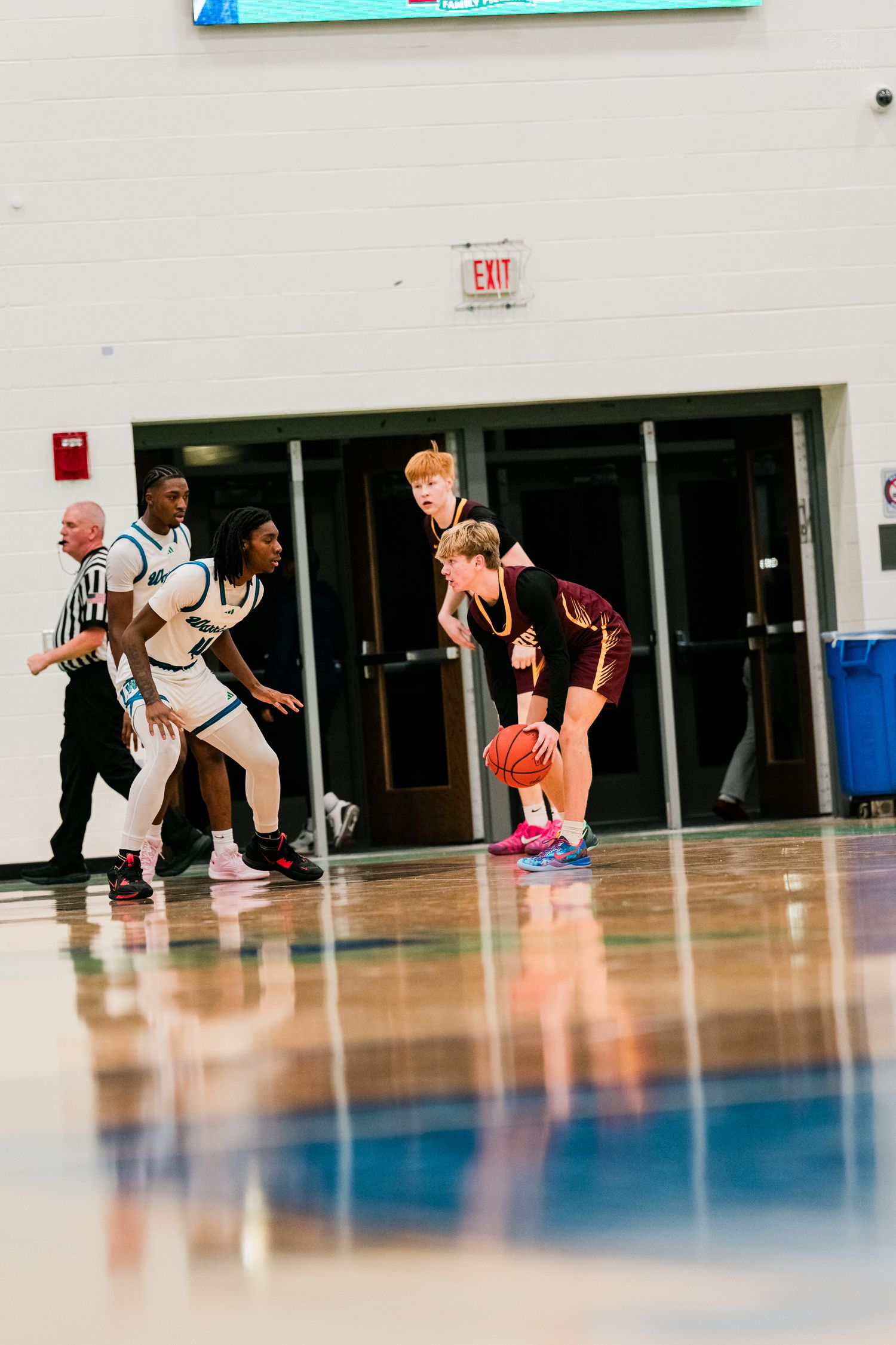 Turpin player dribbles while being defended by Warriors players near the exit door of the gymnasium.