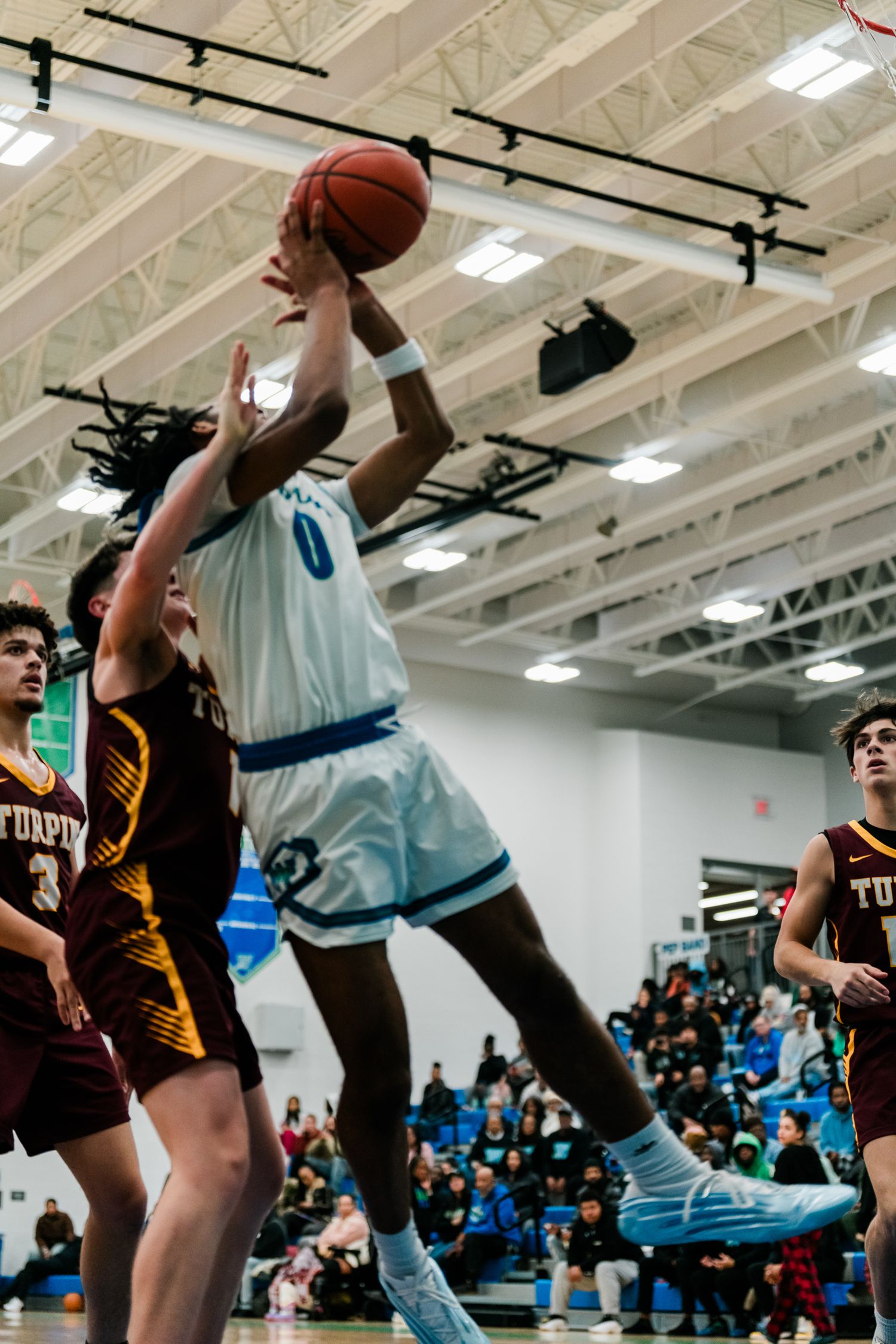 Warriors player number 0 goes up for a contested layup against Turpin defenders during a high school basketball game.