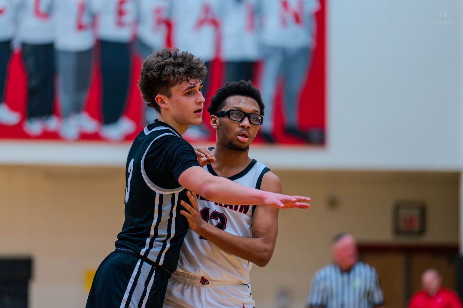 Two high school basketball players battle for position under the basket during a competitive game.