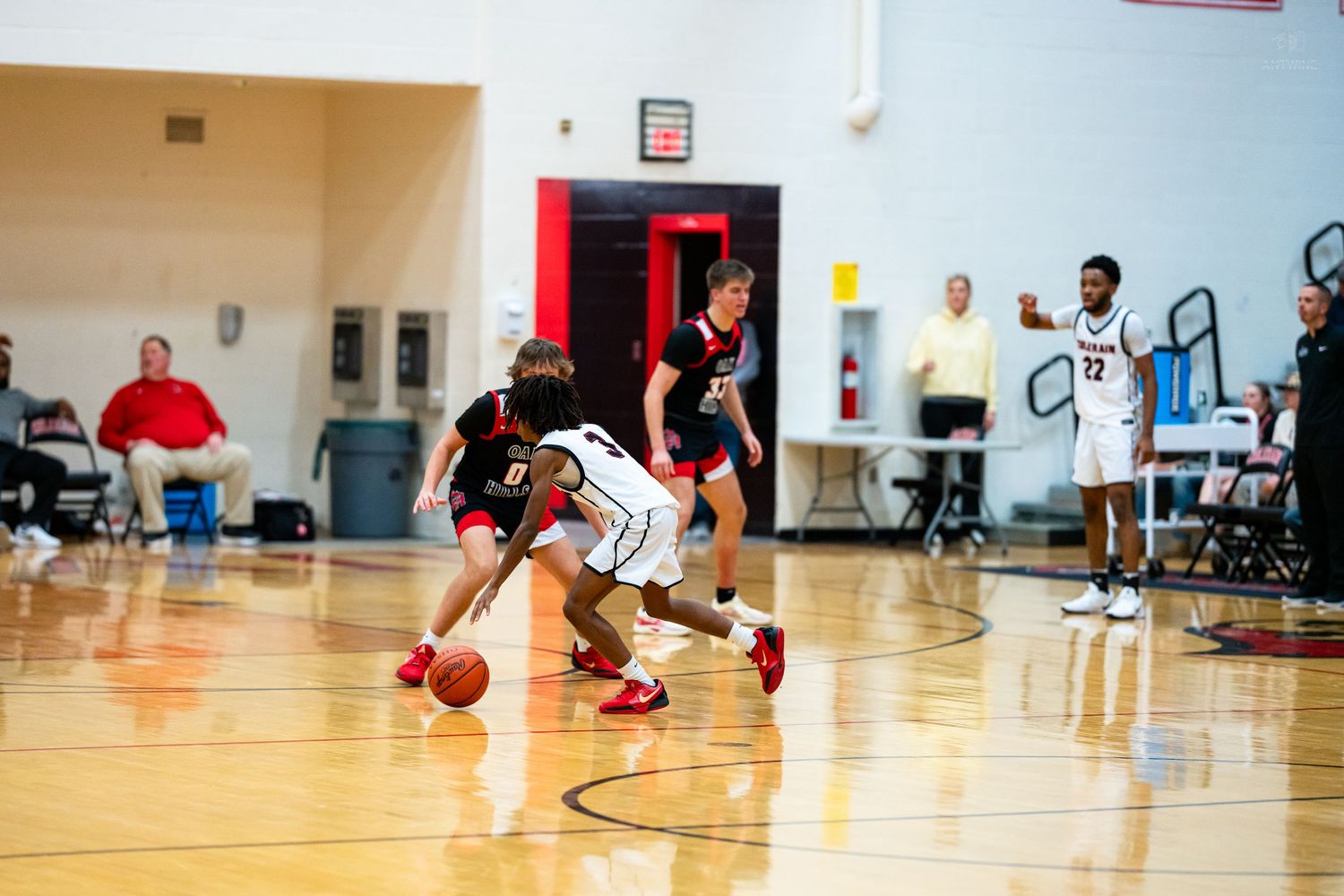 A basketball player dribbles past defenders during a high school game on an indoor court.